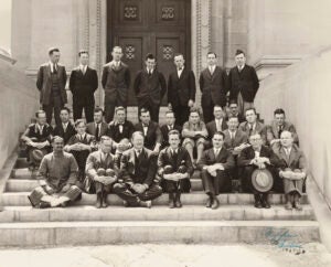 A black and white photo of several rows of men posing for a group portrait on the steps of a building.