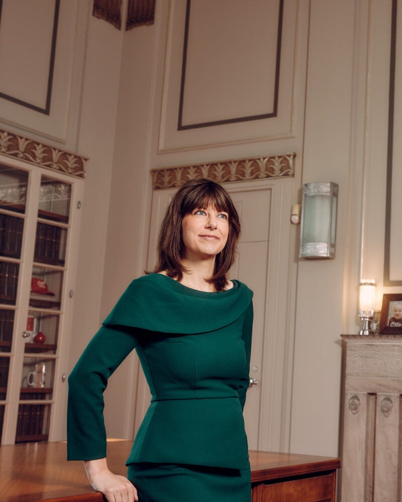 A woman leaning against a desk in a spacious office near a painting of Ruth Bader Ginsburg