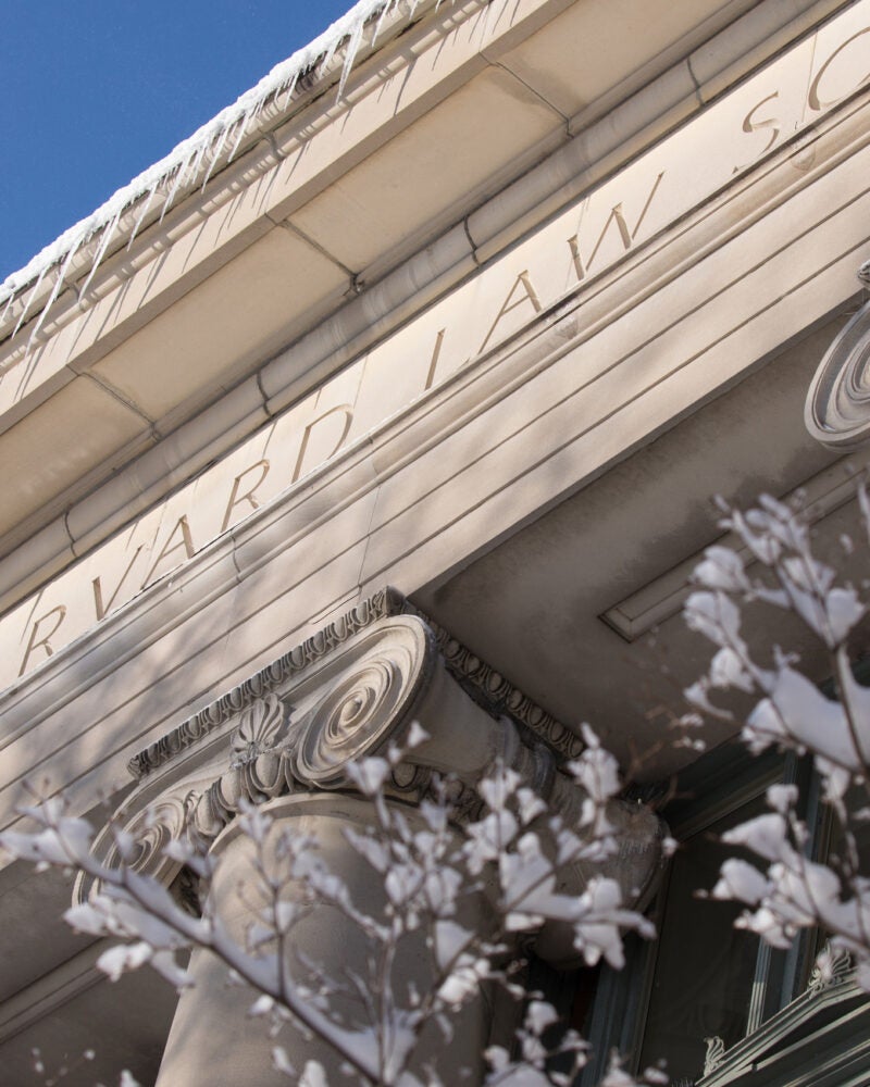 The top of Langdell Hall with the words Harvard Law School etched in the stone and snow covered branches in front.