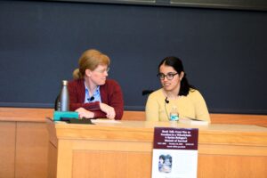 two women speak on a panel in a classroom