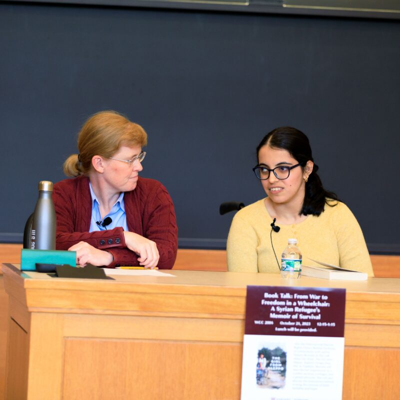 two women speak on a panel in a classroom