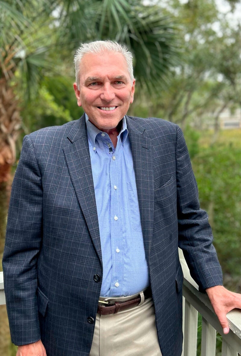 A portrait of a man standing outside near a fence.