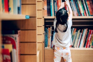 Small child choosing books from a bookshelf.