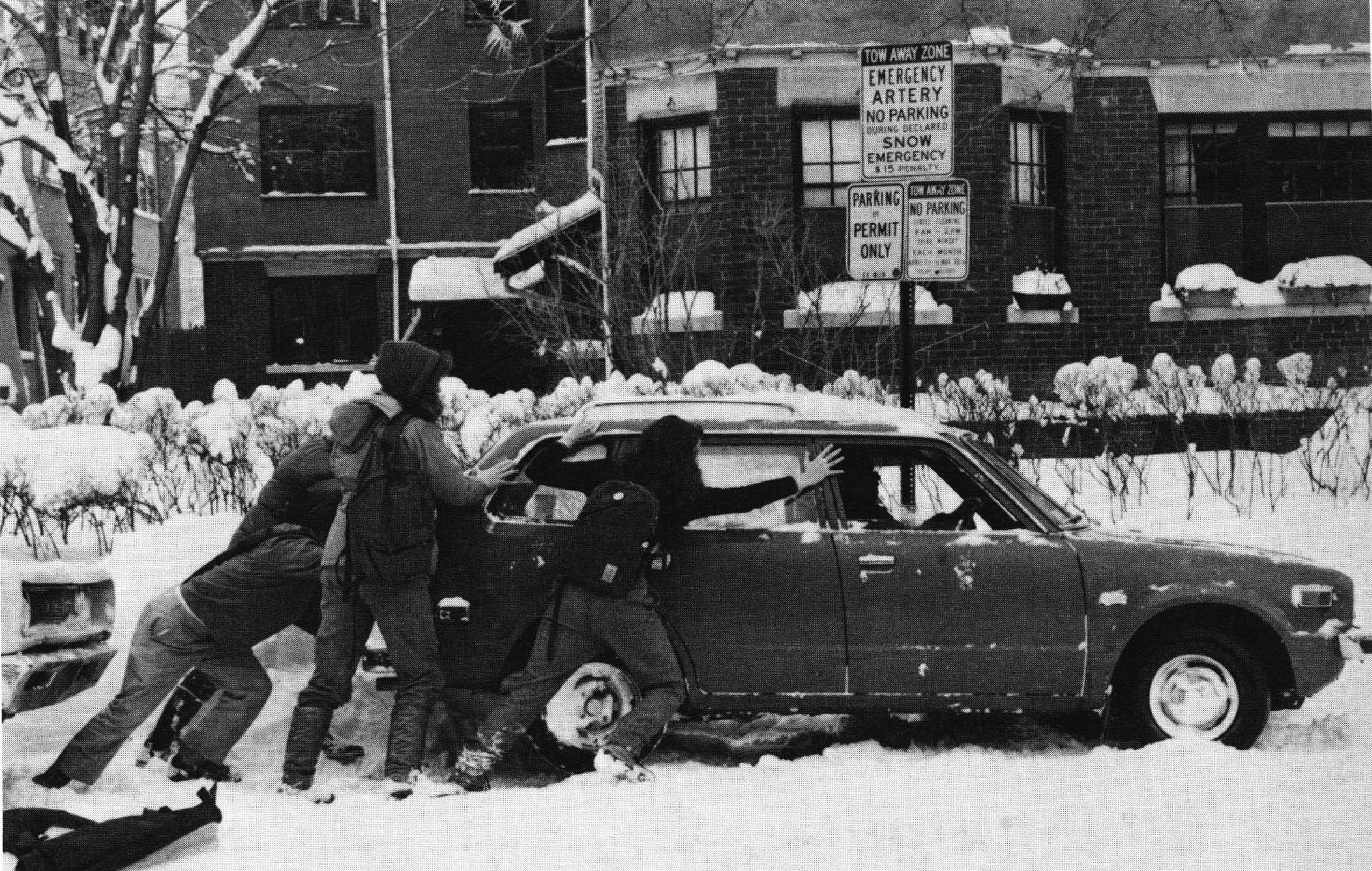A black and white photo of students pushing a car out of a snow drift