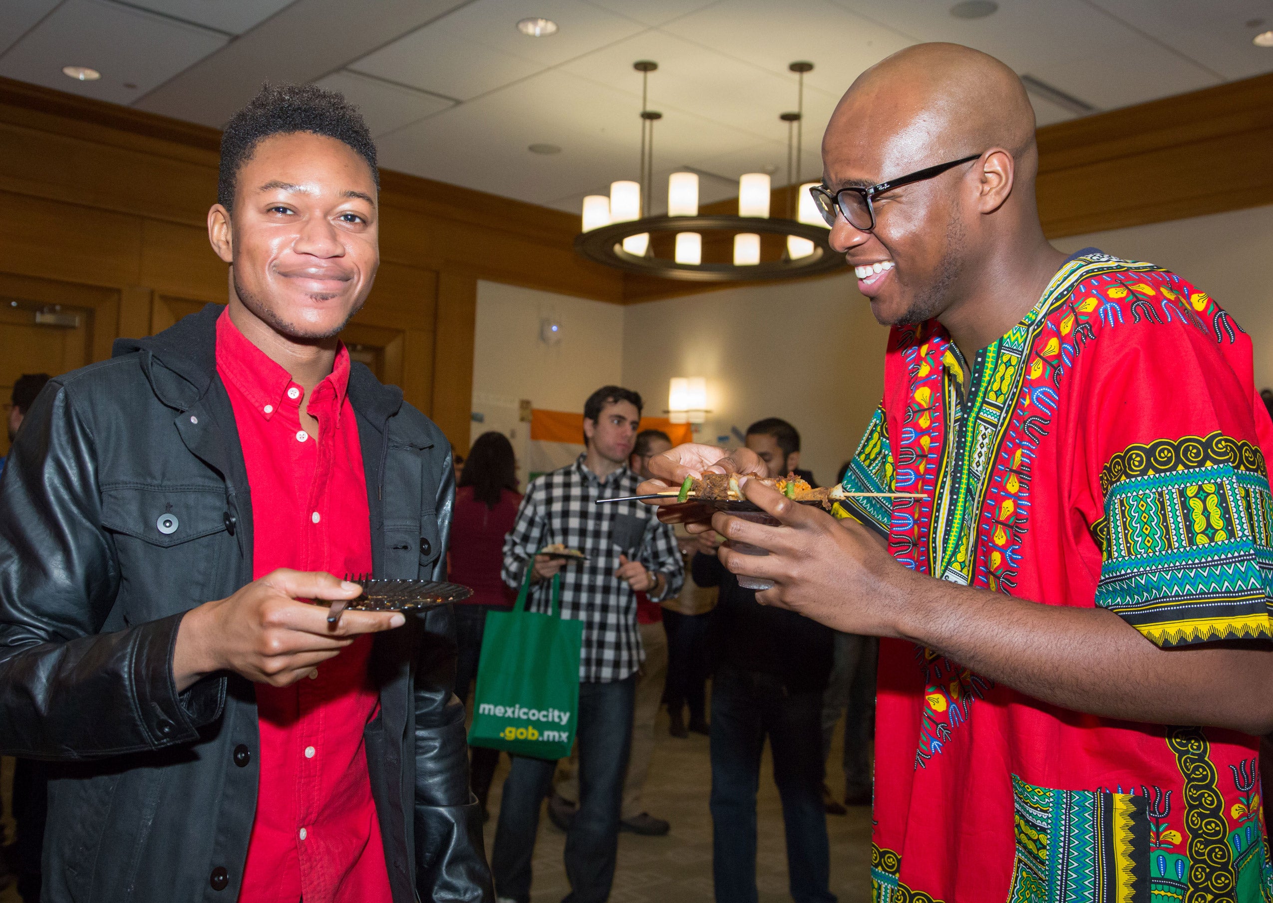 Two men standing, smiling and eating