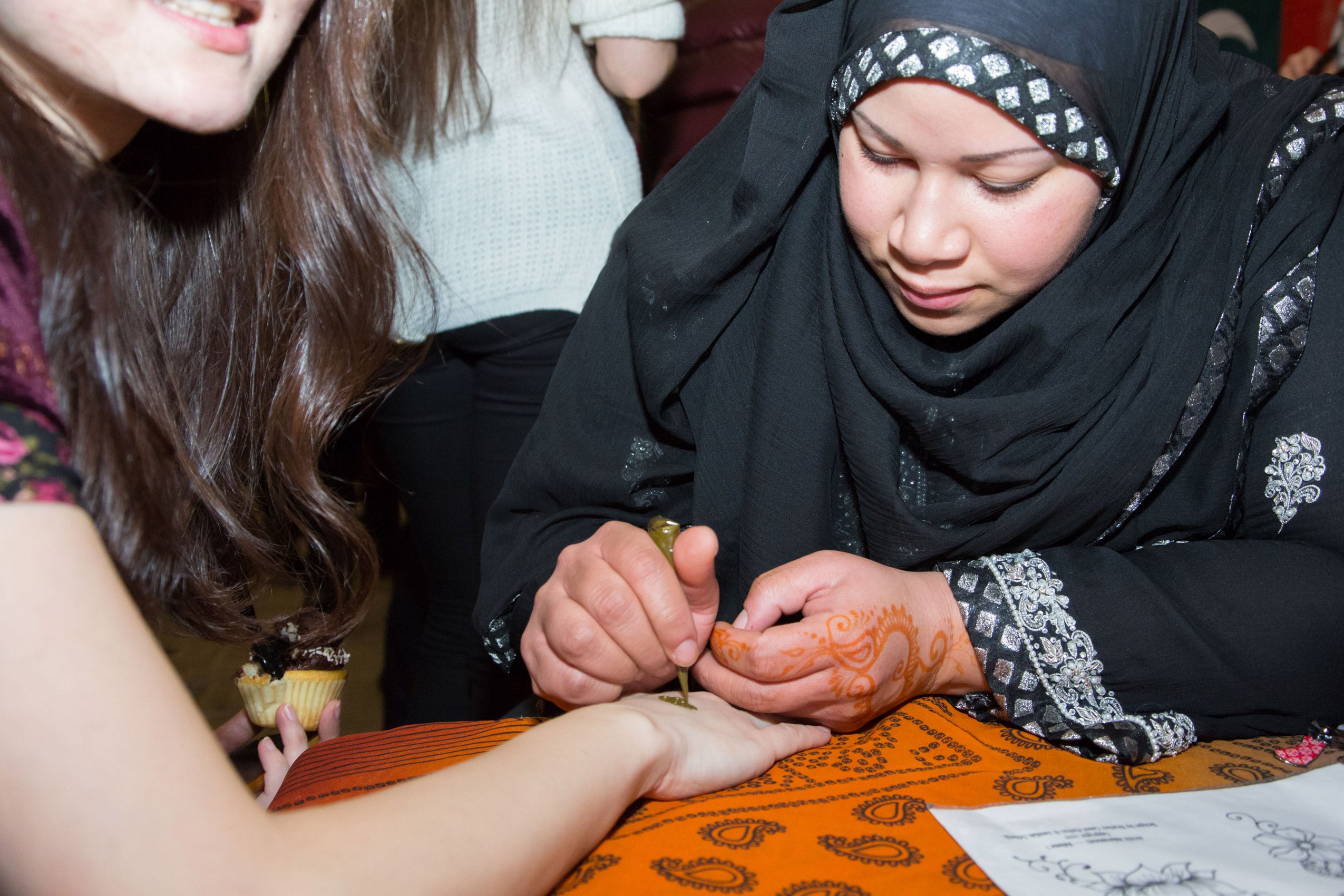 A woman decorating the hand of another woman with henna