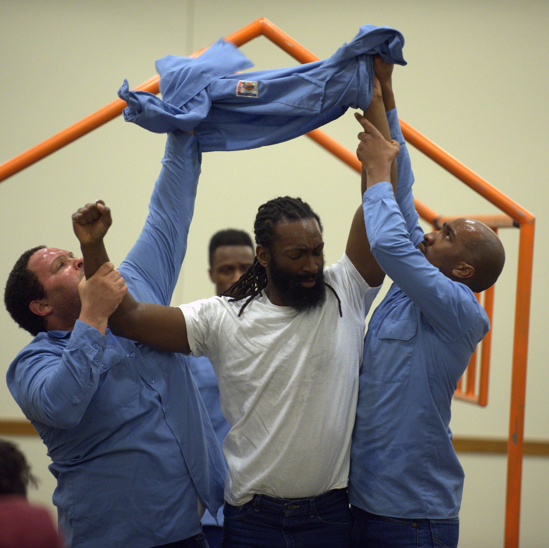 A man standing behind three other men, two of whom are removing the coat from the third