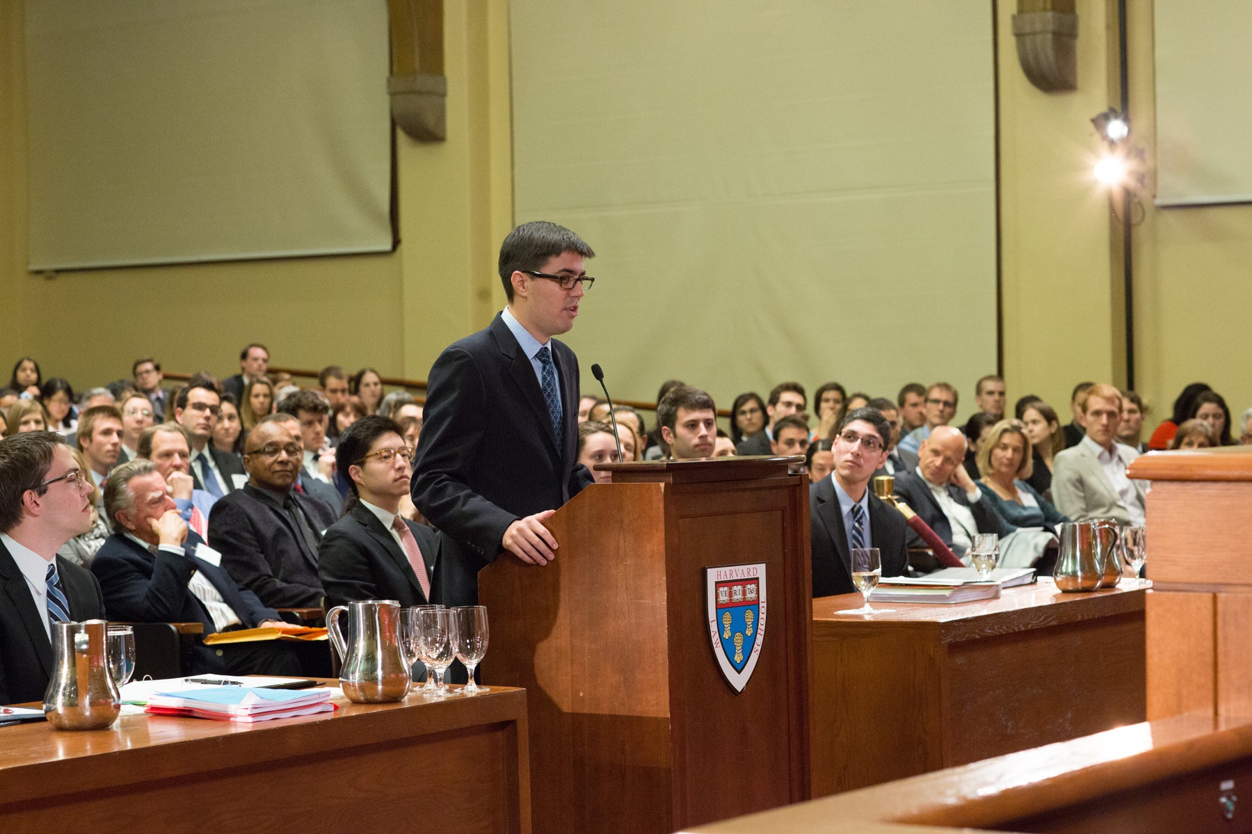 someone speaking at a podium with a large audience behind him