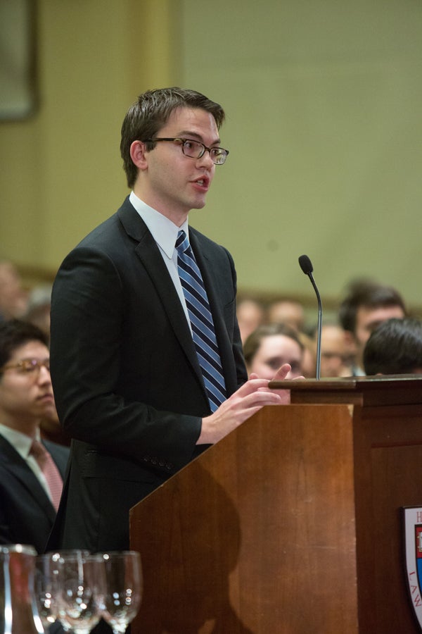 Someone speaking at a podium with a crowd behind him