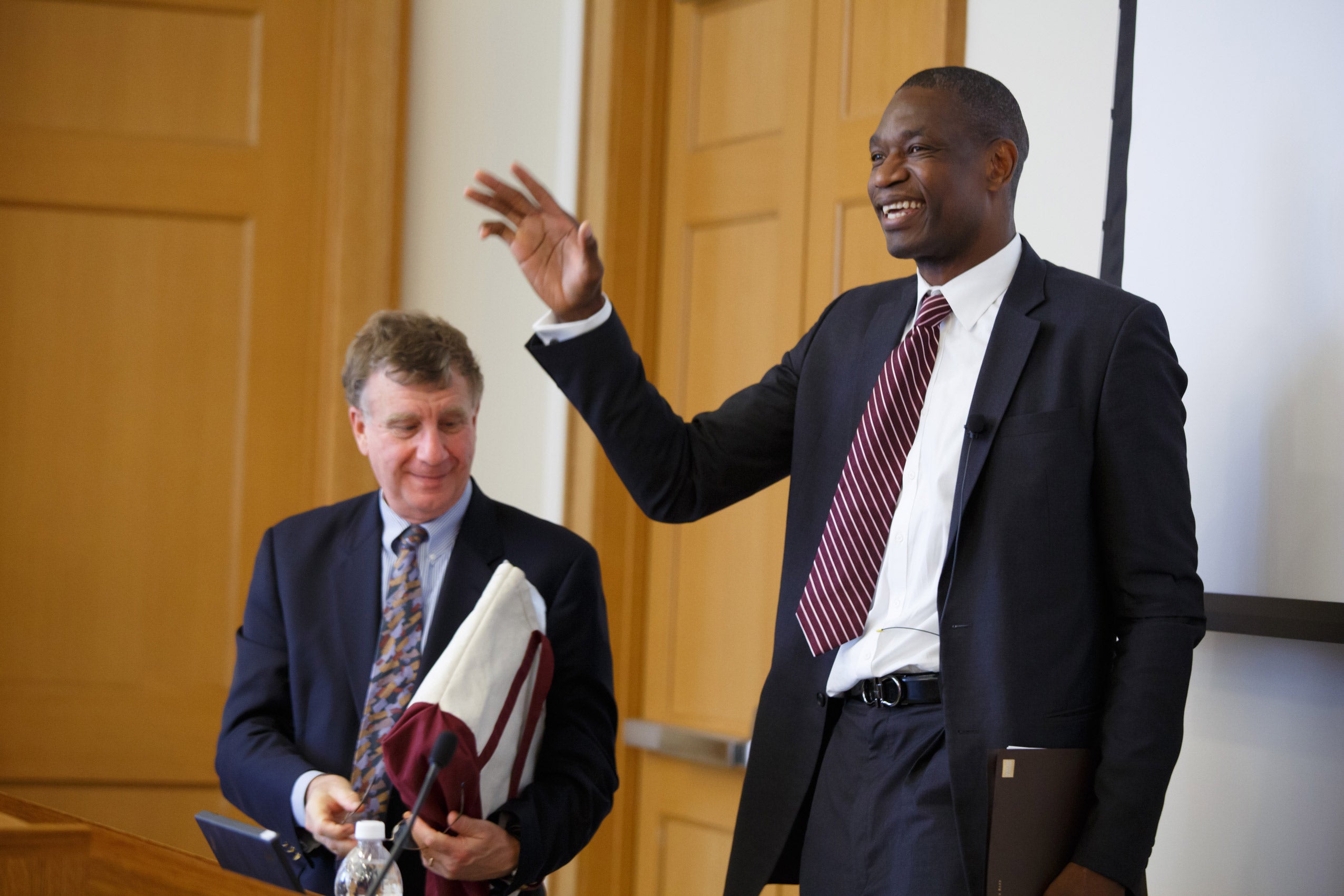 A man speaking into a microphone with another man standing next to him
