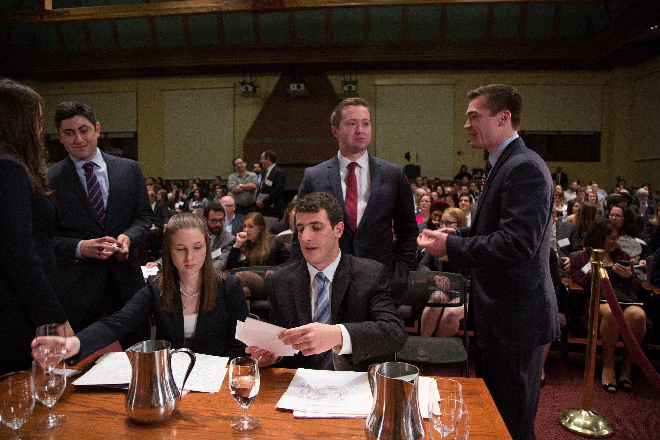Students conferring over documents as more students look on from the audience