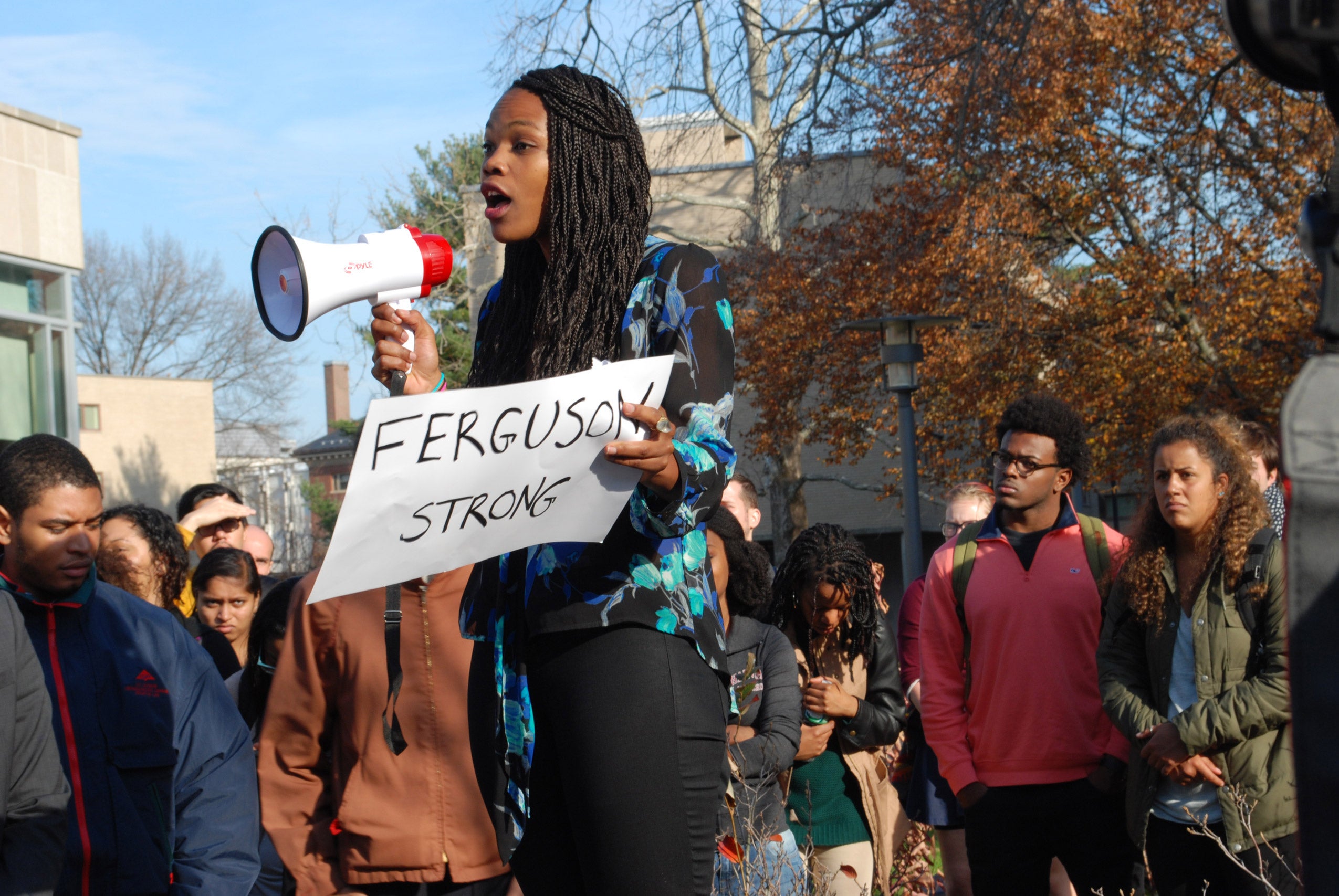 A woman speaking into a megaphone and holding a protest sign that reads 'Ferguson Strong'