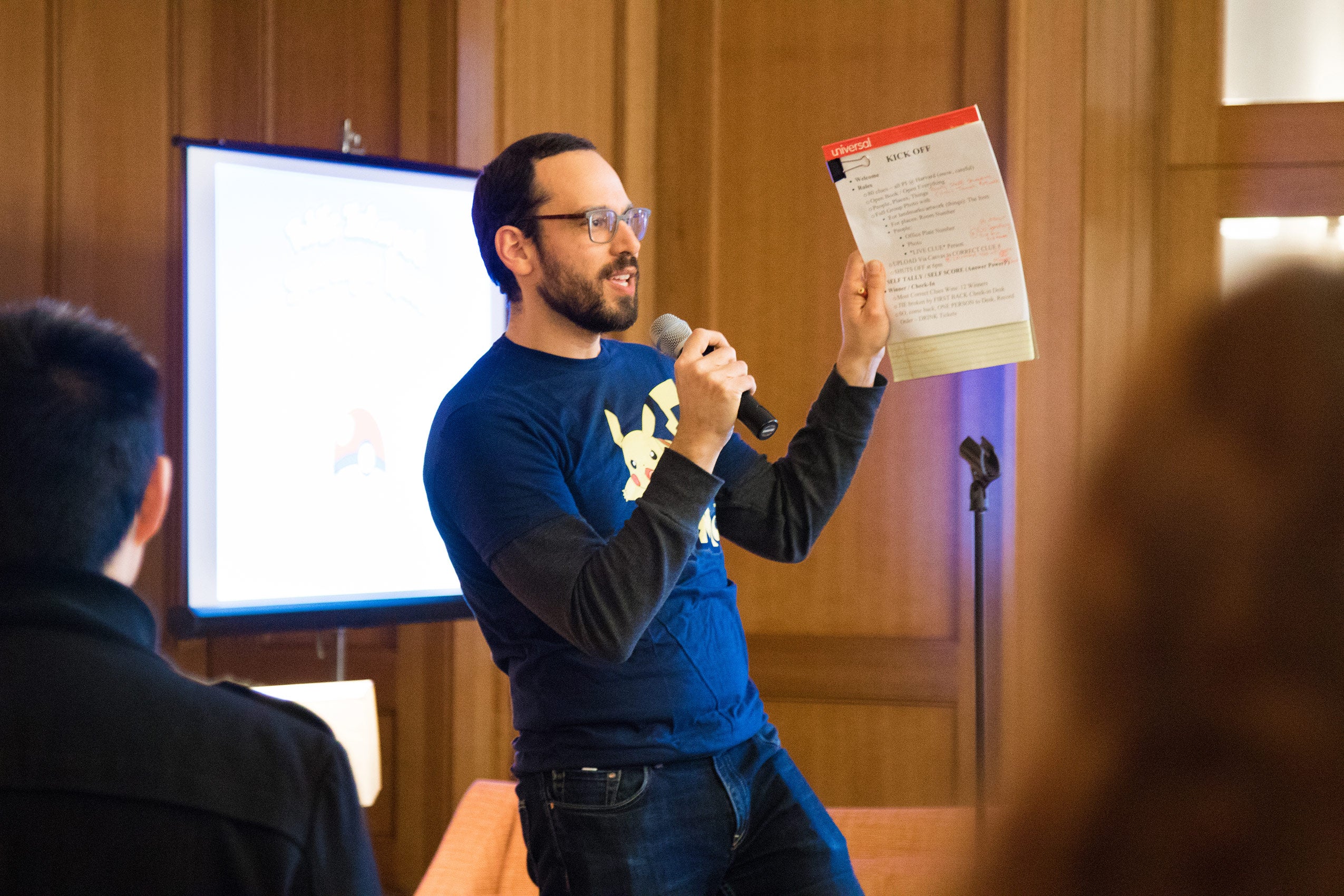 A man holding a microphone and a notepad, speaking