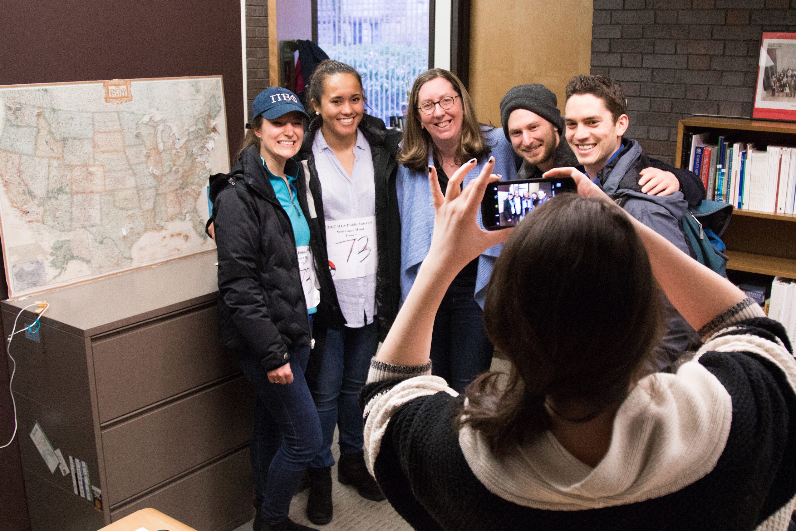 A woman taking a photo on a cellphone of a group of three women and two men