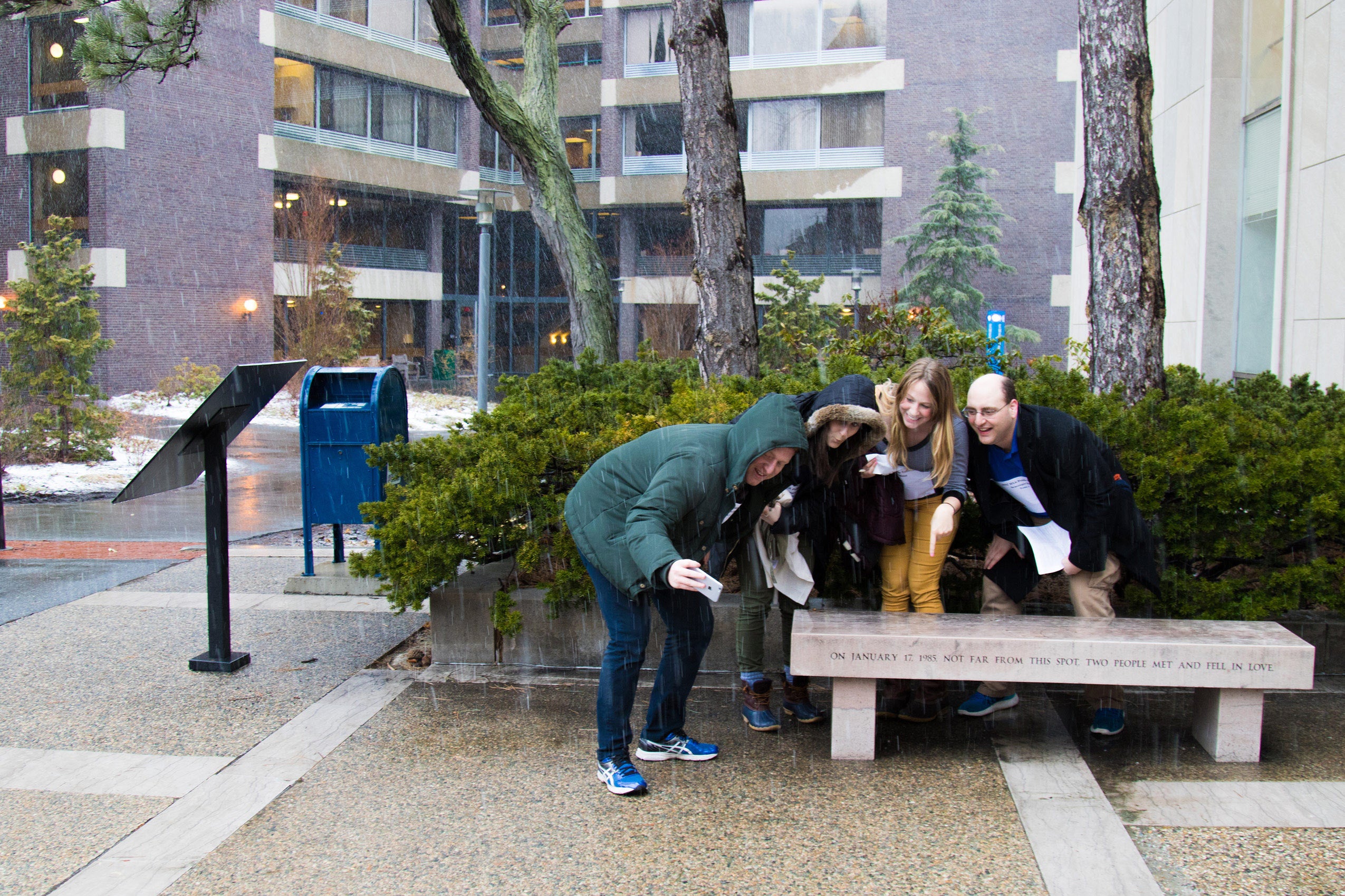 Four students taking a selfie with a bench outside the Lewis Center