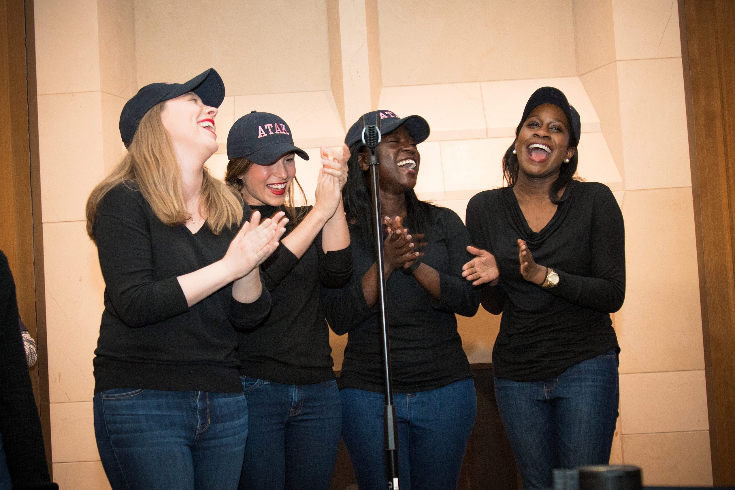 Four women in matching outfits standing in front of a microphone, singing