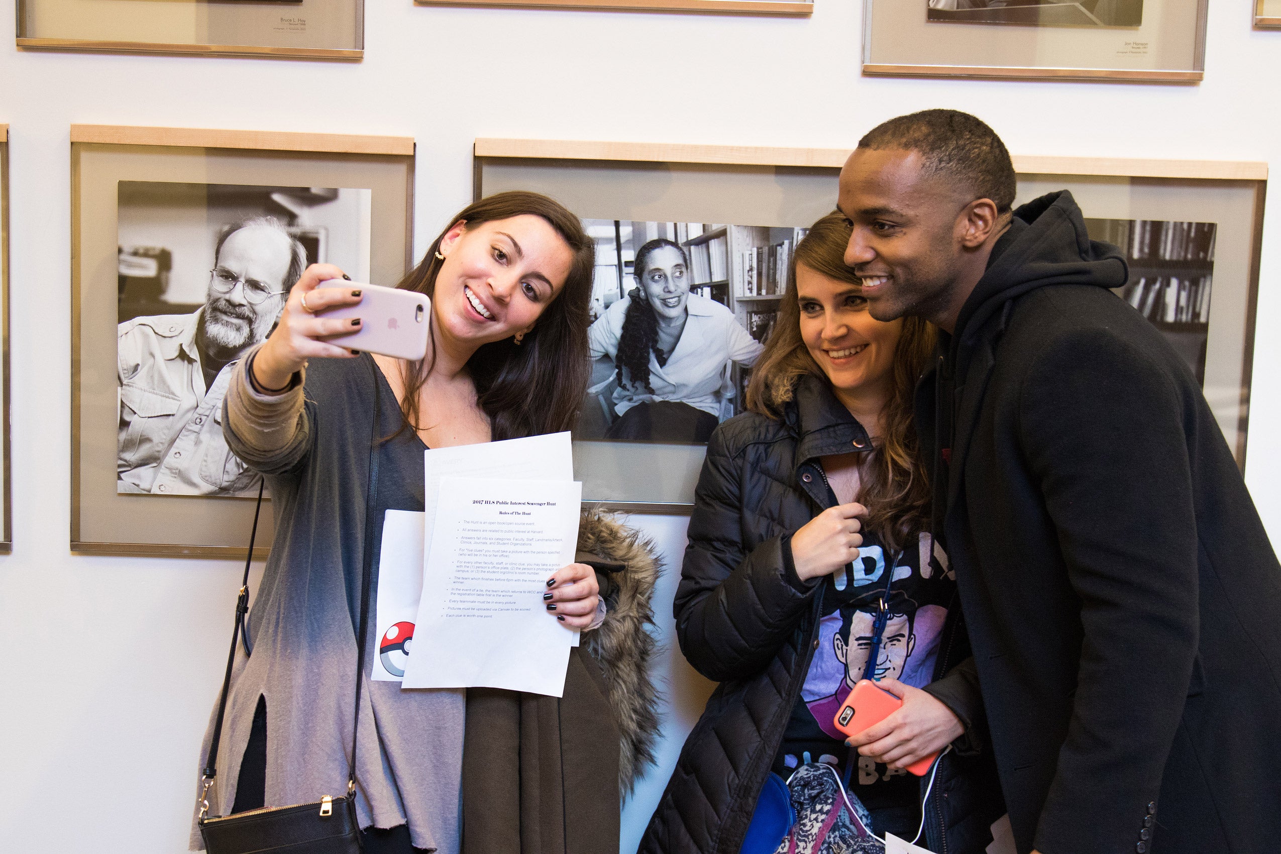 Two women and a man taking a selfie with a faculty wall portrait