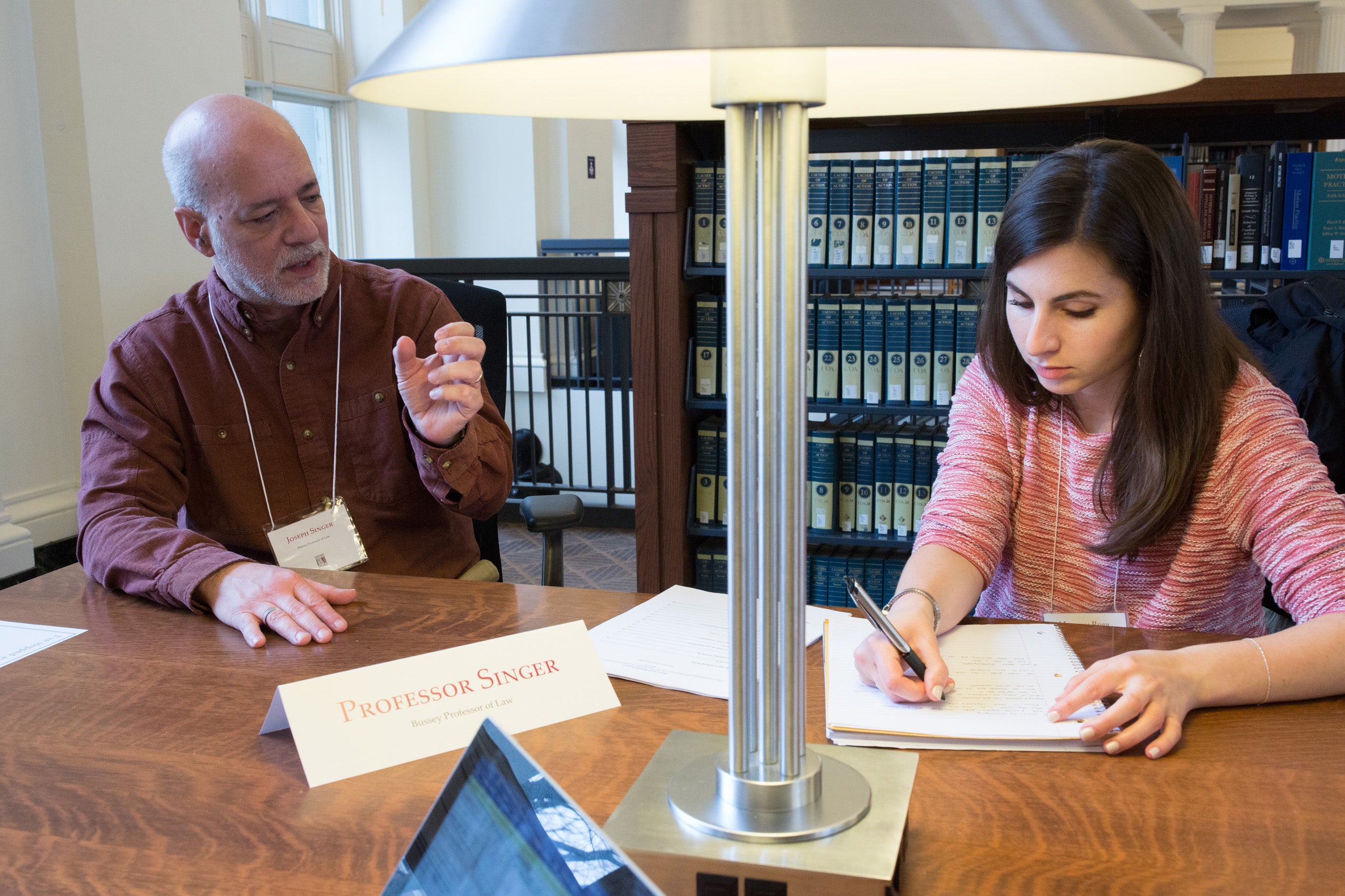 A man and a woman seated at a table - the woman writes as the man speaks