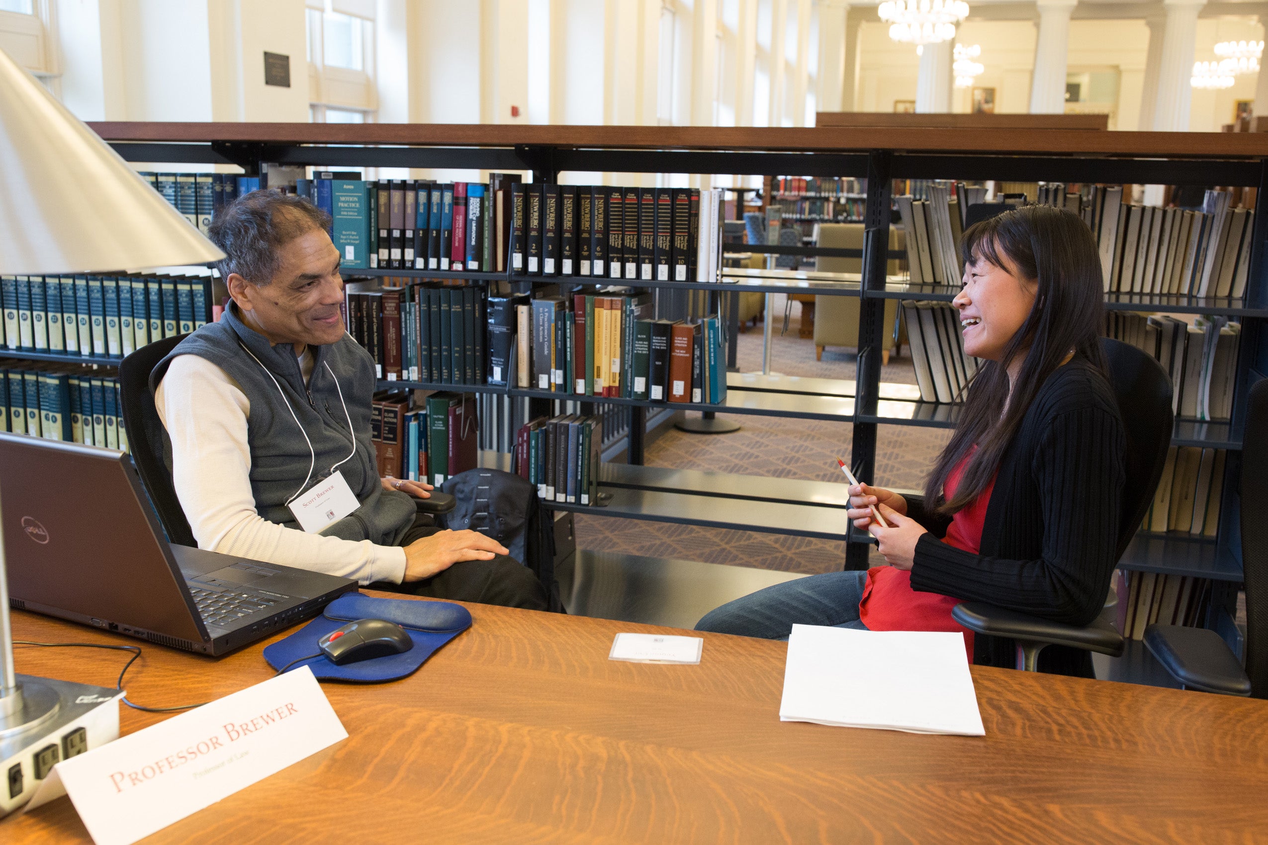 A man and a woman sitting at a table in front of library stacks, having a conversation