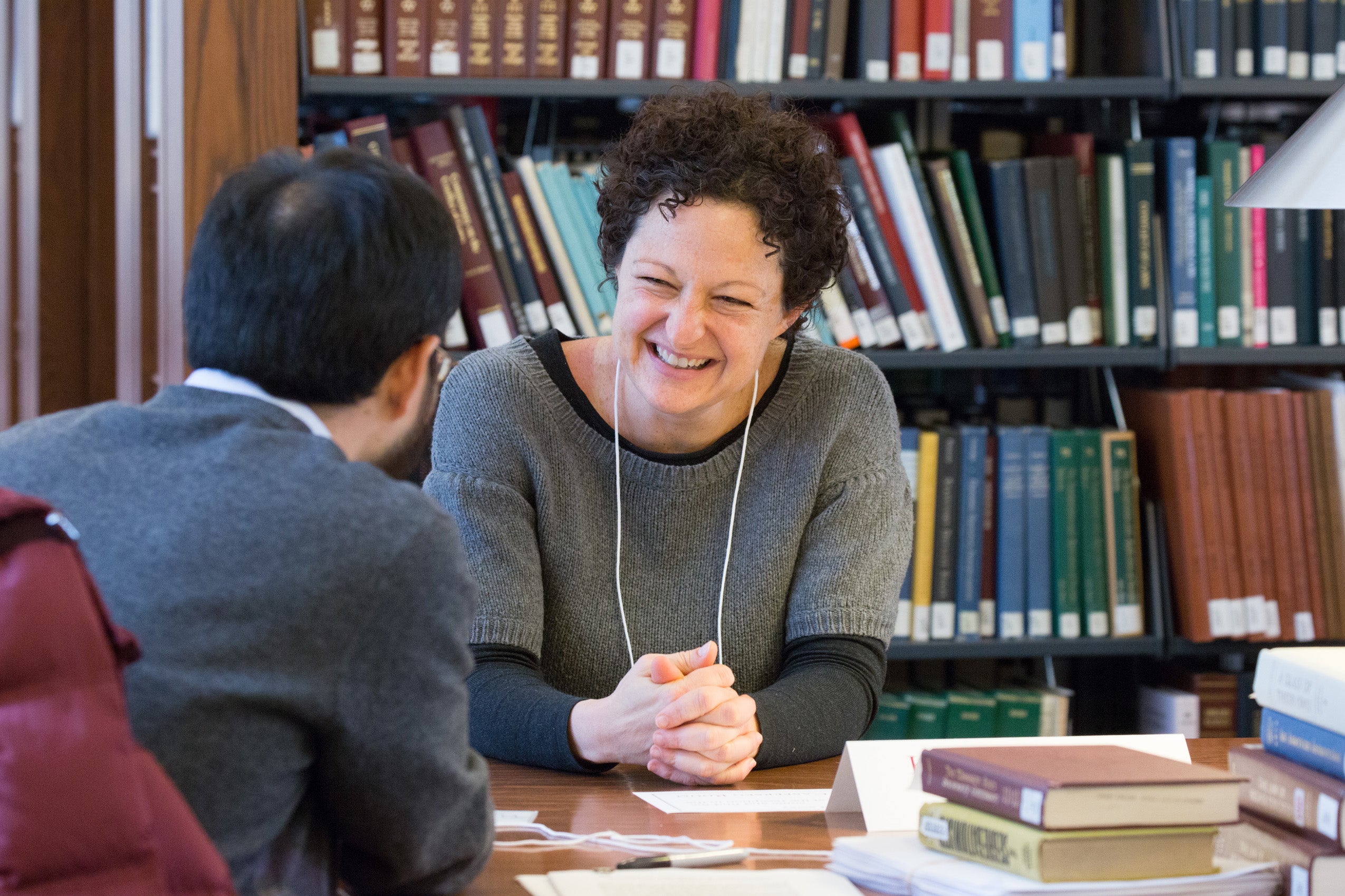 A man and a woman seated at a table in front of a library stack having a conversation