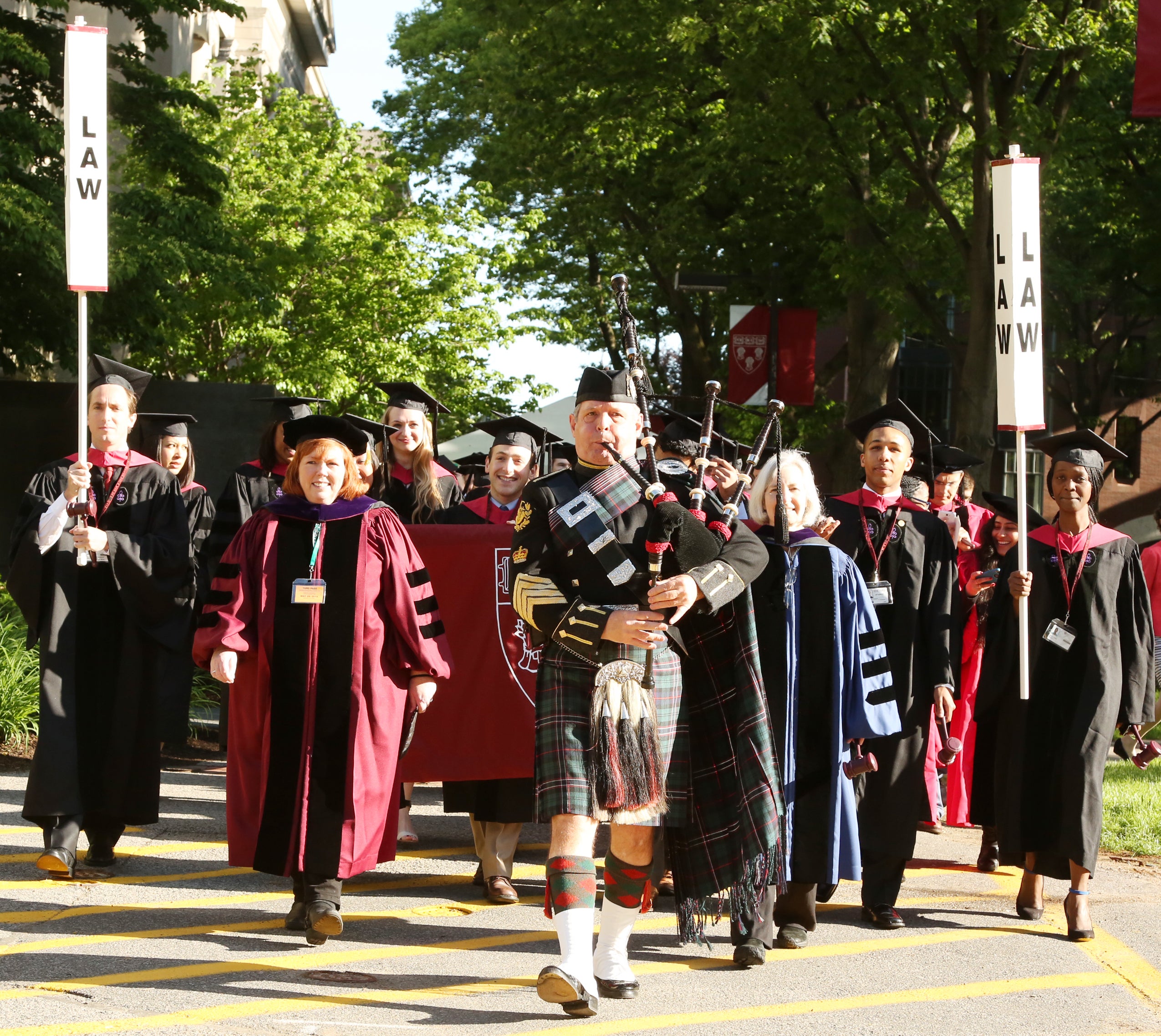A bagpiper playing and leading a procession of students on Holmes Field