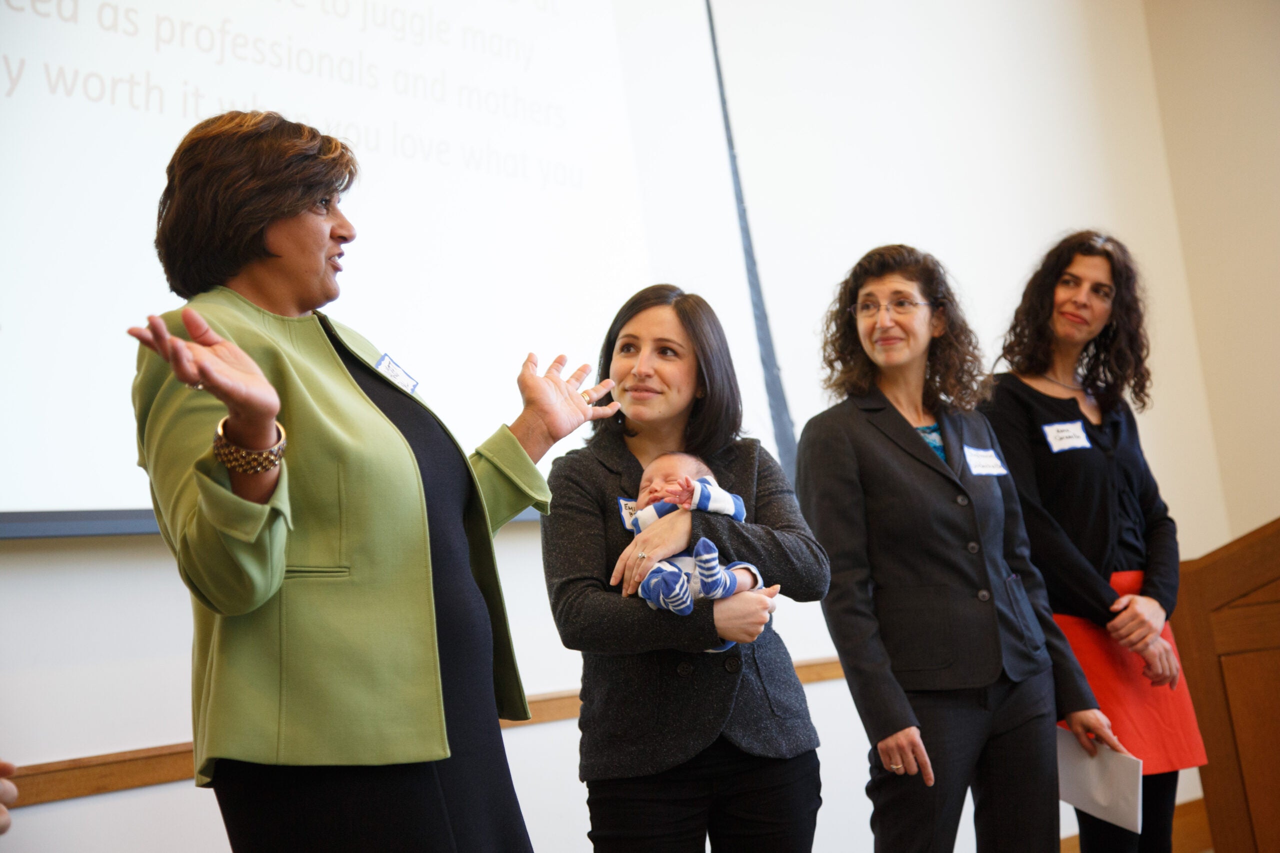 Four women, one holding a baby, standing together at the front of a room
