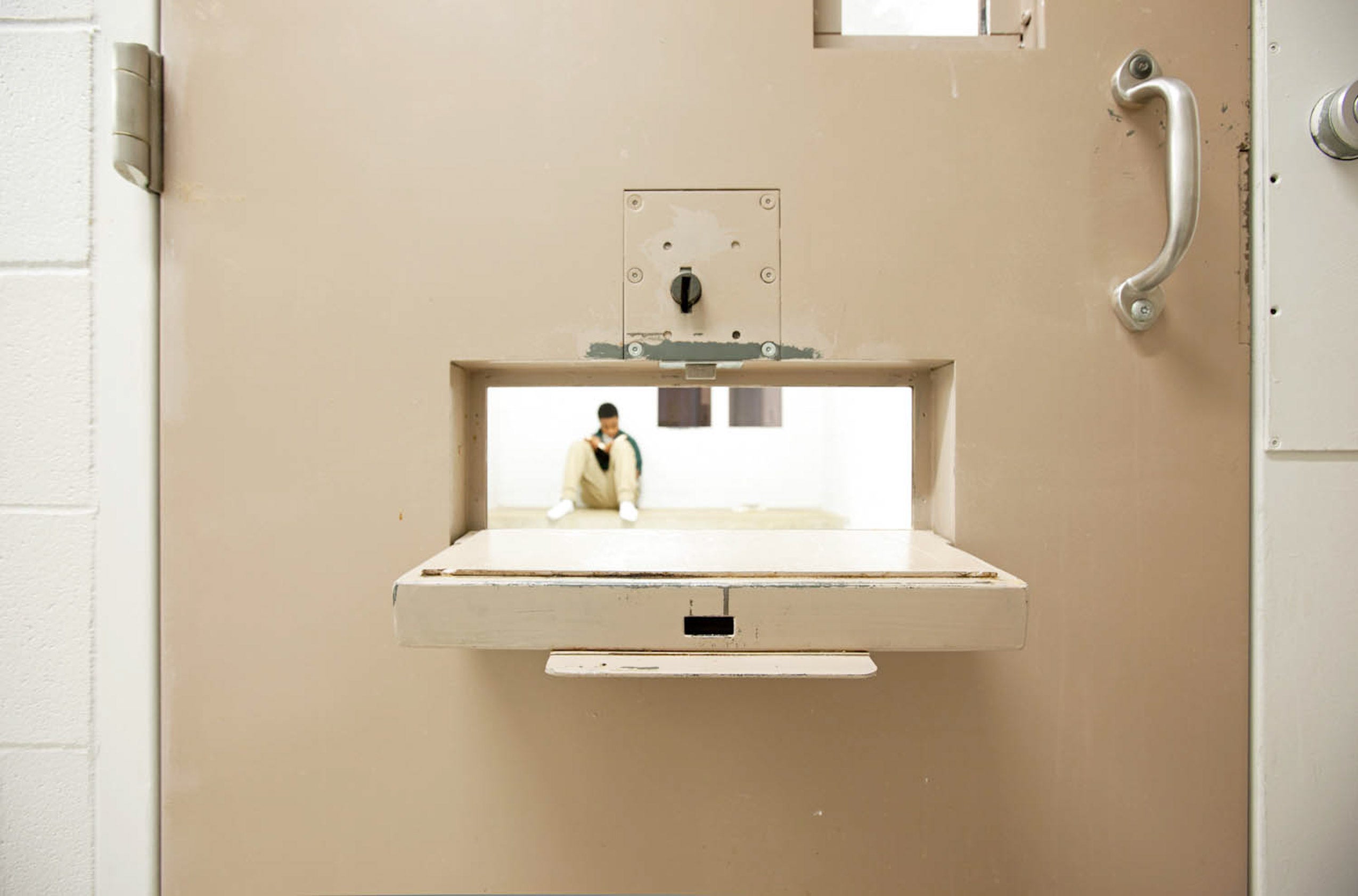 A boy sitting in isolation, seen through a slot in the door