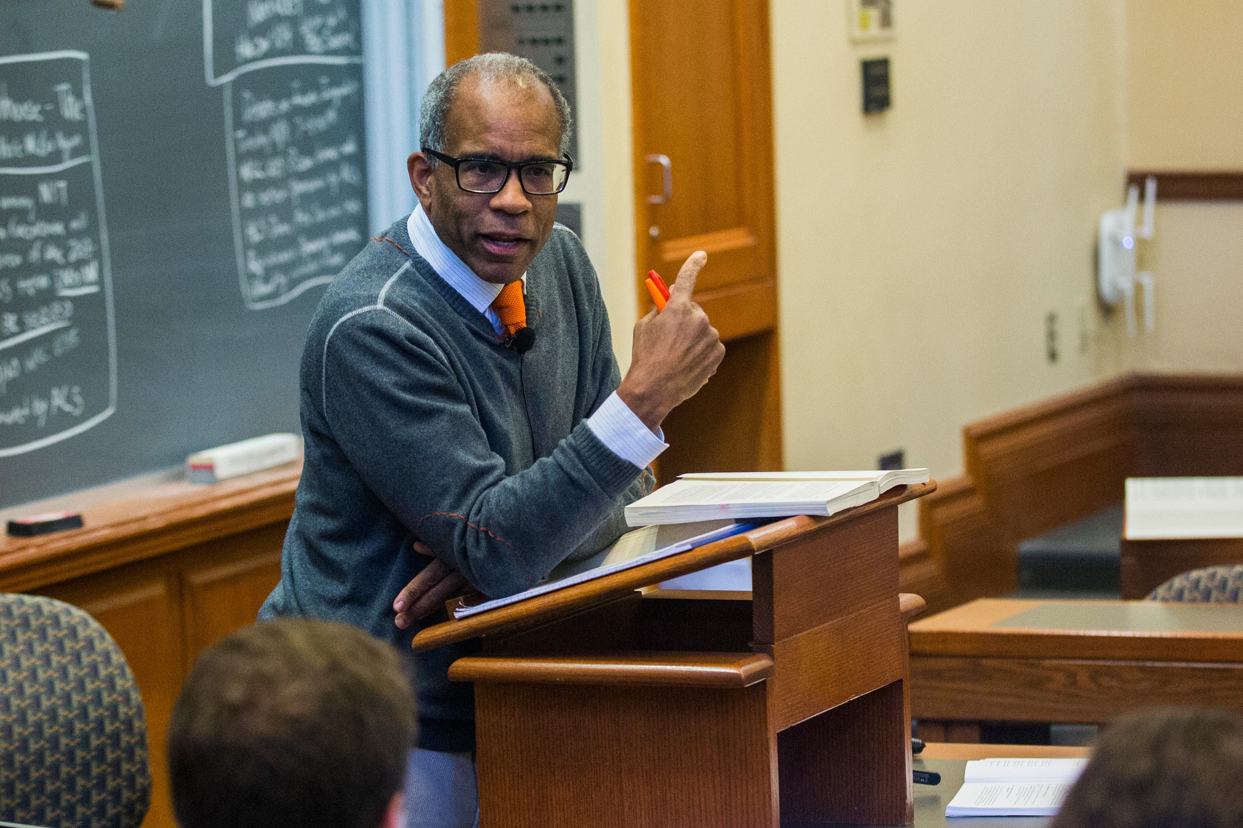 A man leaning on a podium at the front of a classroom giving a lecture