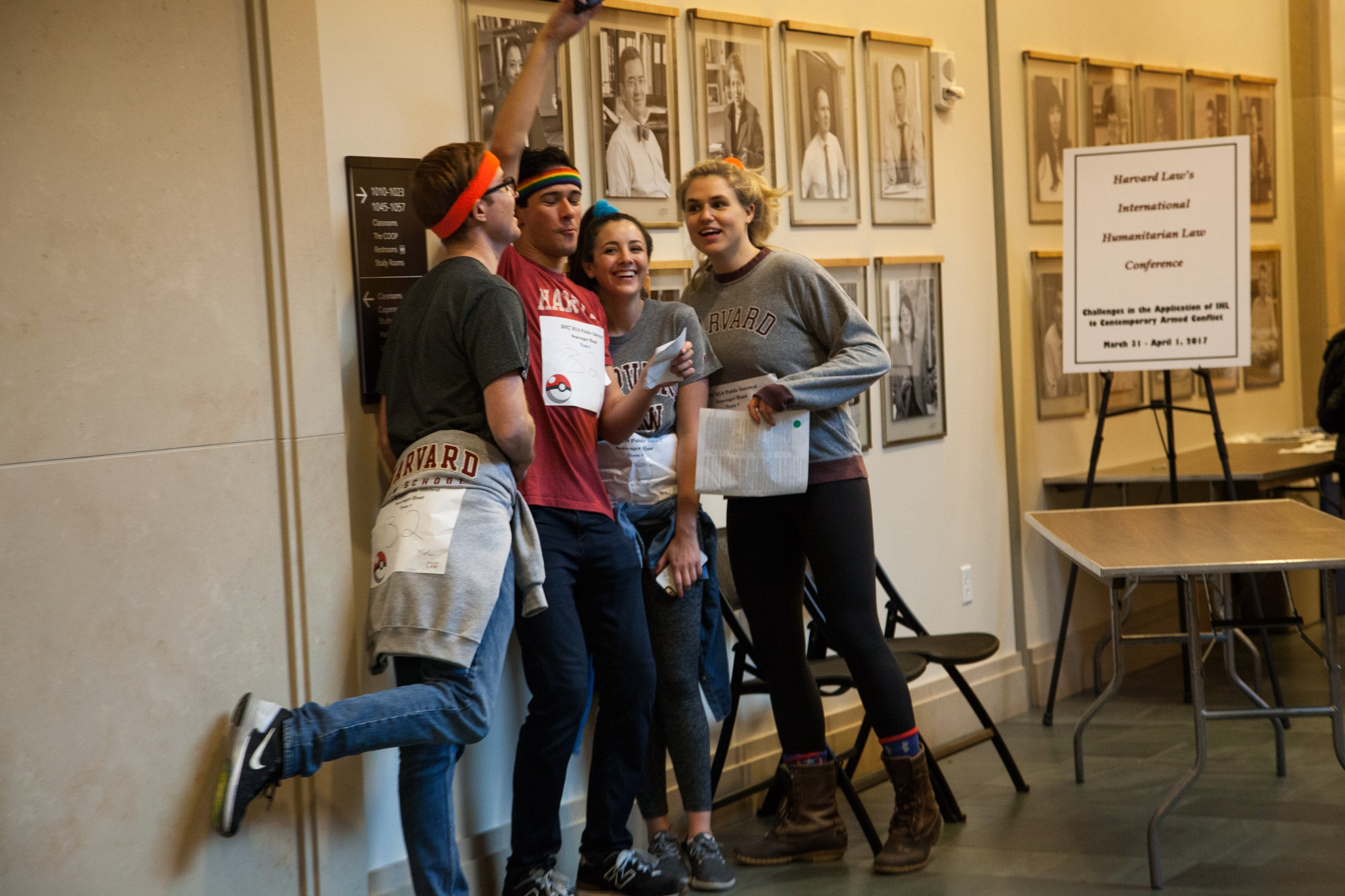 Four students posing in front of some of the faculty wall portraits