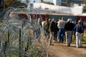Barb wire fence with people in background.
