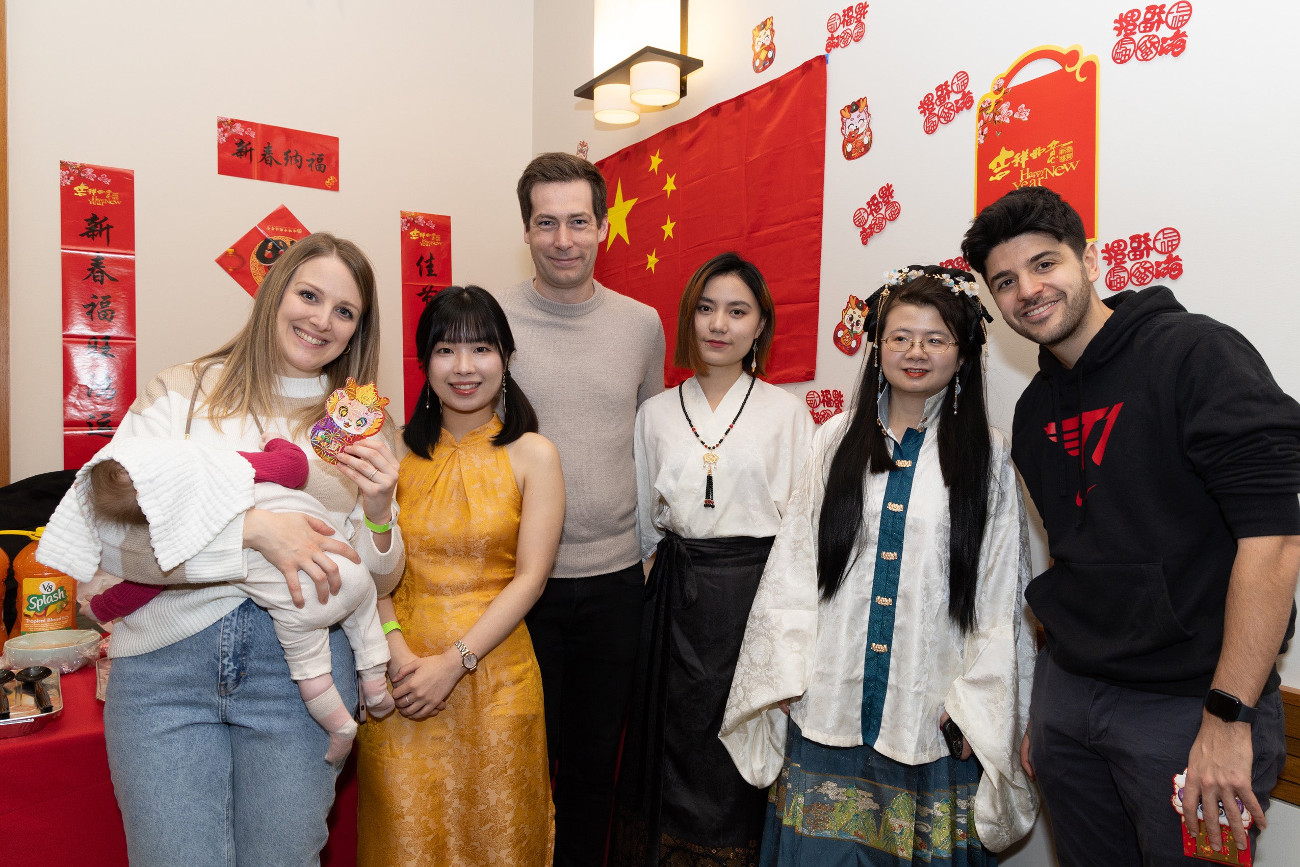 A group of students pose in front a wall of colorful international flags.