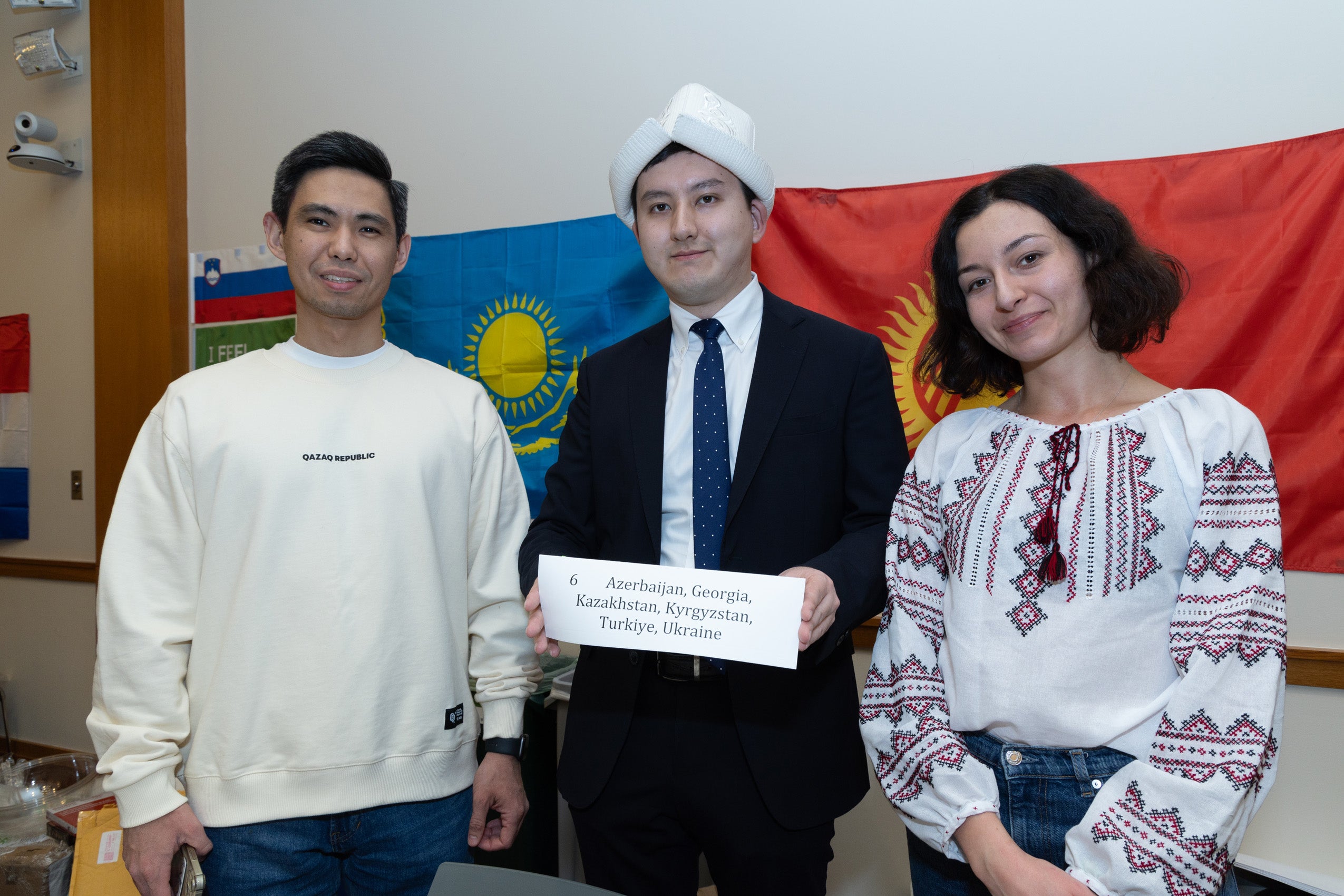 Three students stand in front of an international flag at an event