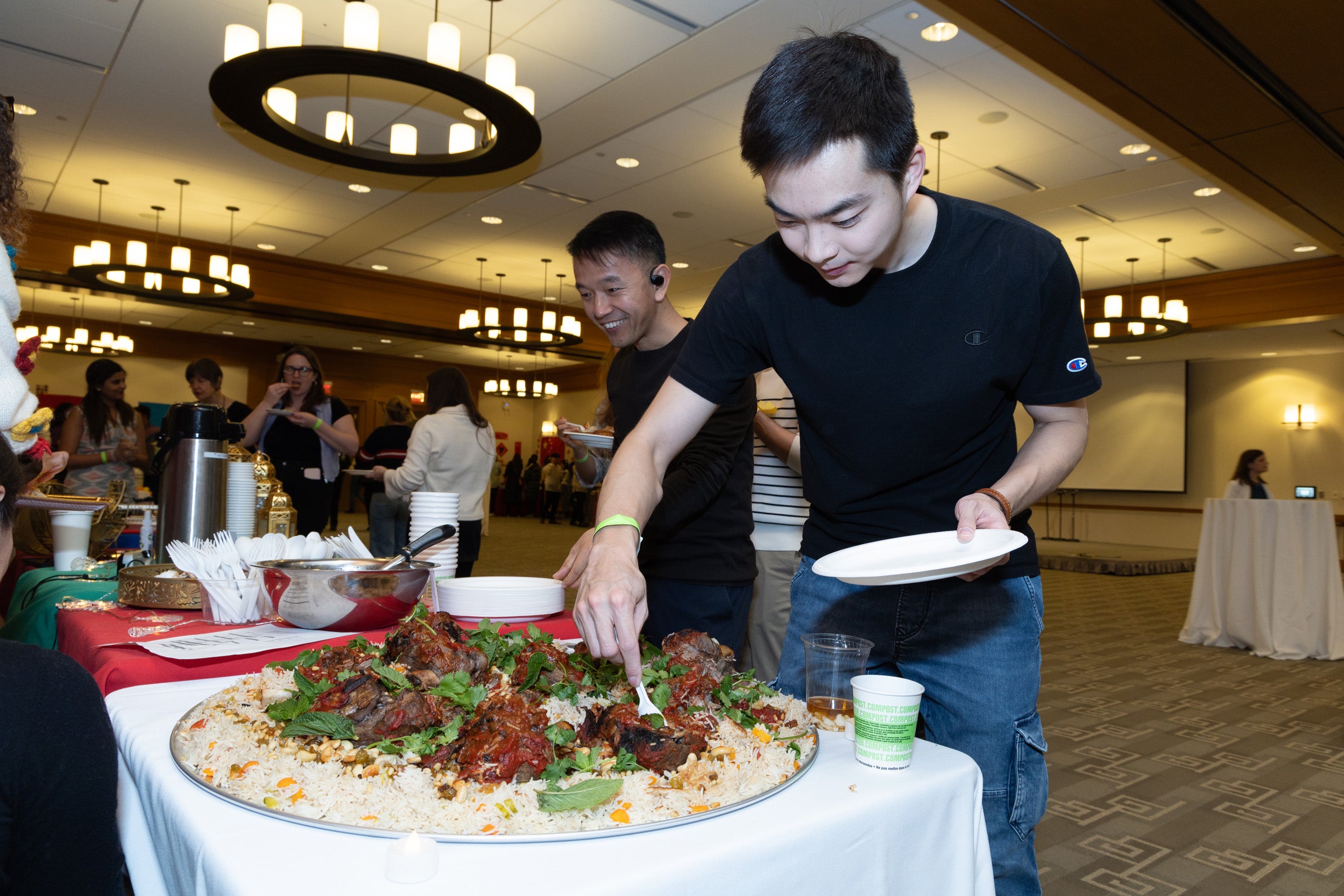 A man standing at a table at an event fills is dish with food