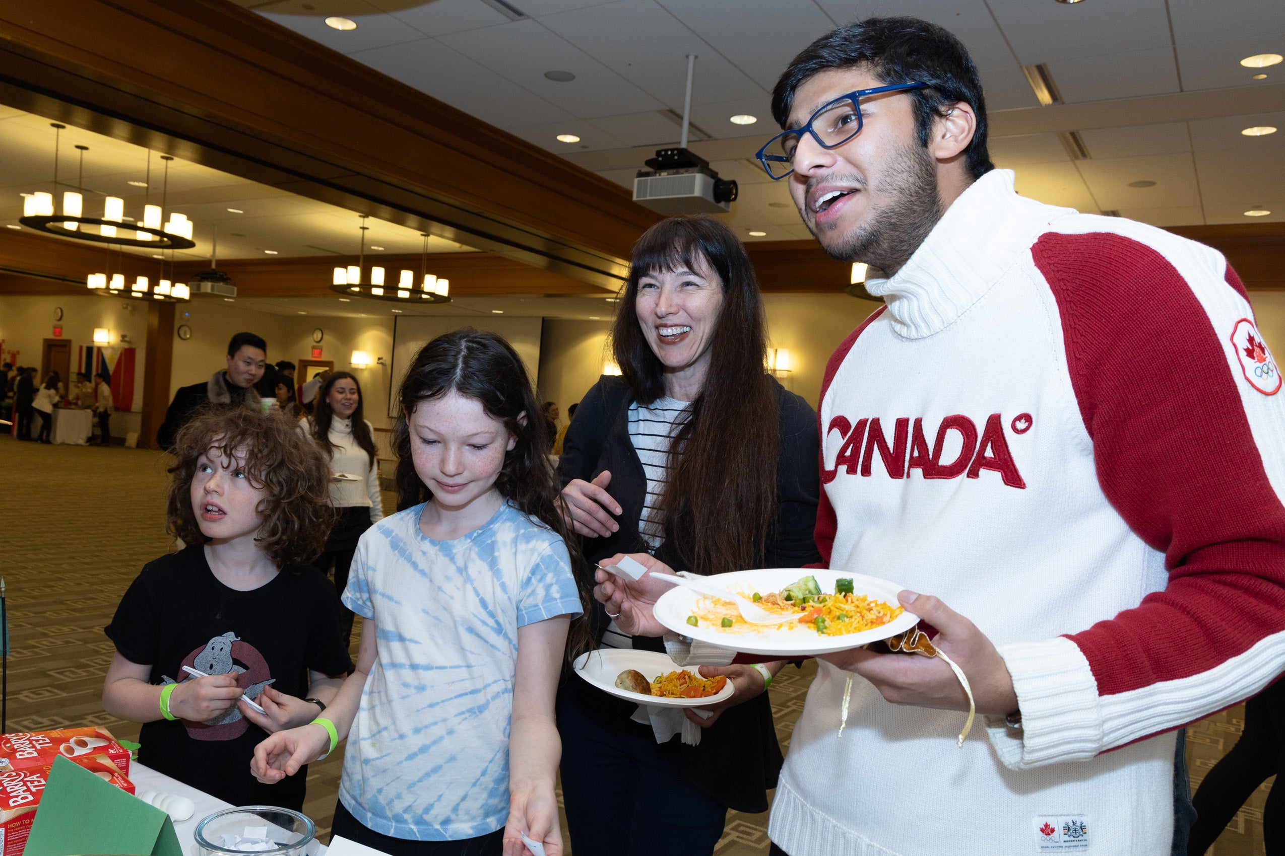Two young children and their mom and a student fill their plates with food at an event.