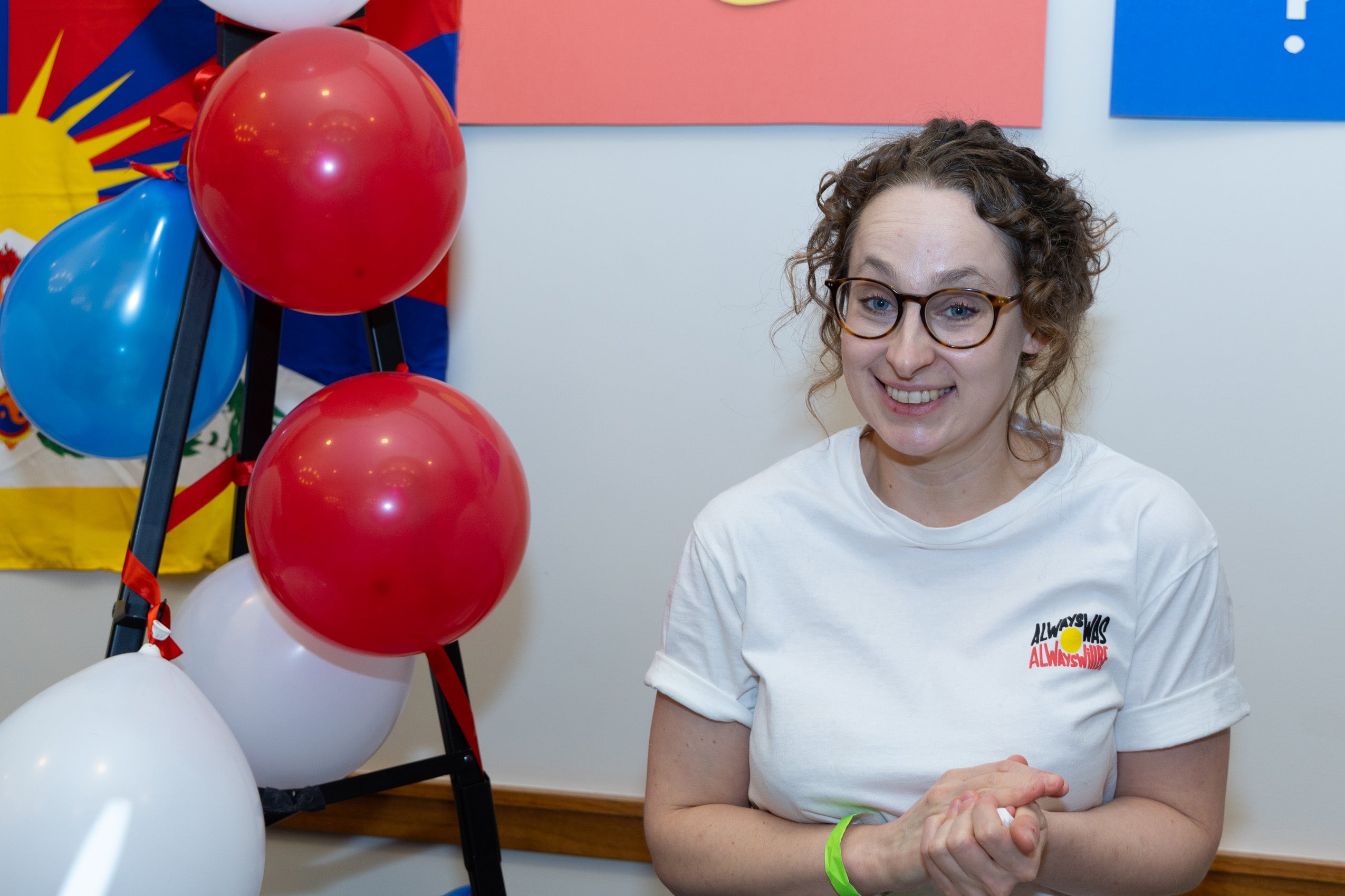 A women stands behind a table with red white and blue balloons to her left.