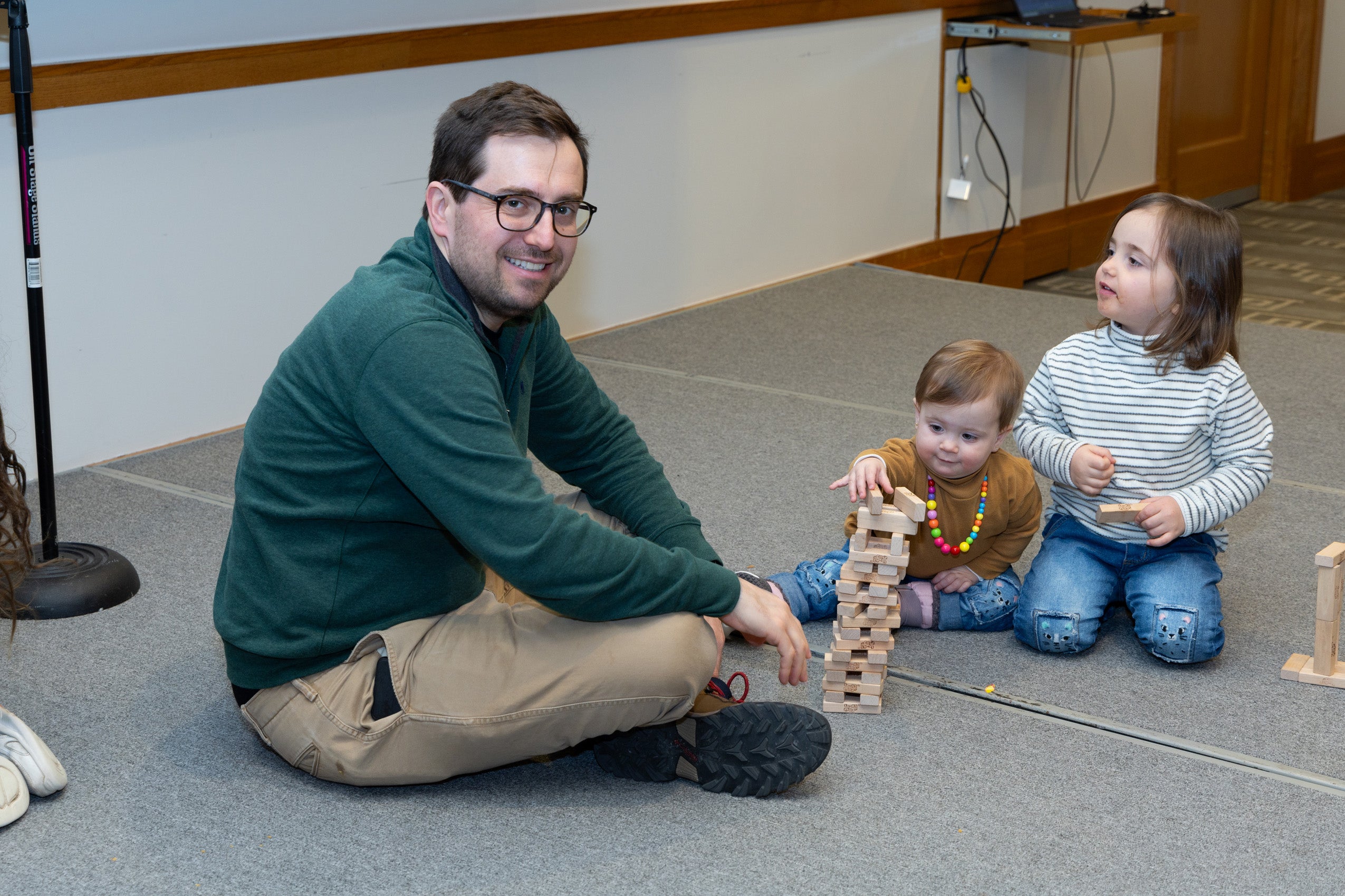A man sits on the ground with two young children playing with blocks.