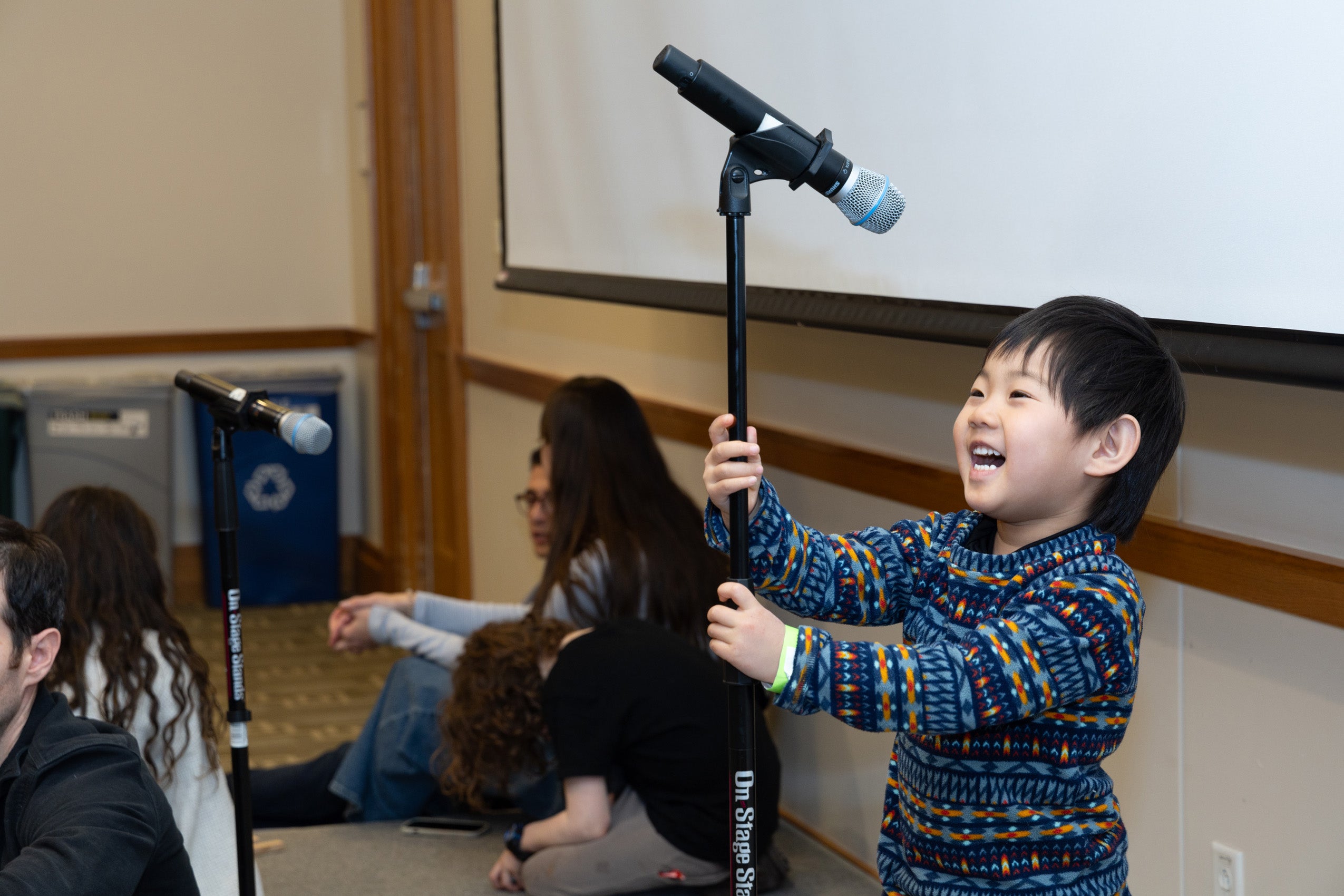 A small boy holds a microphone twice his height.