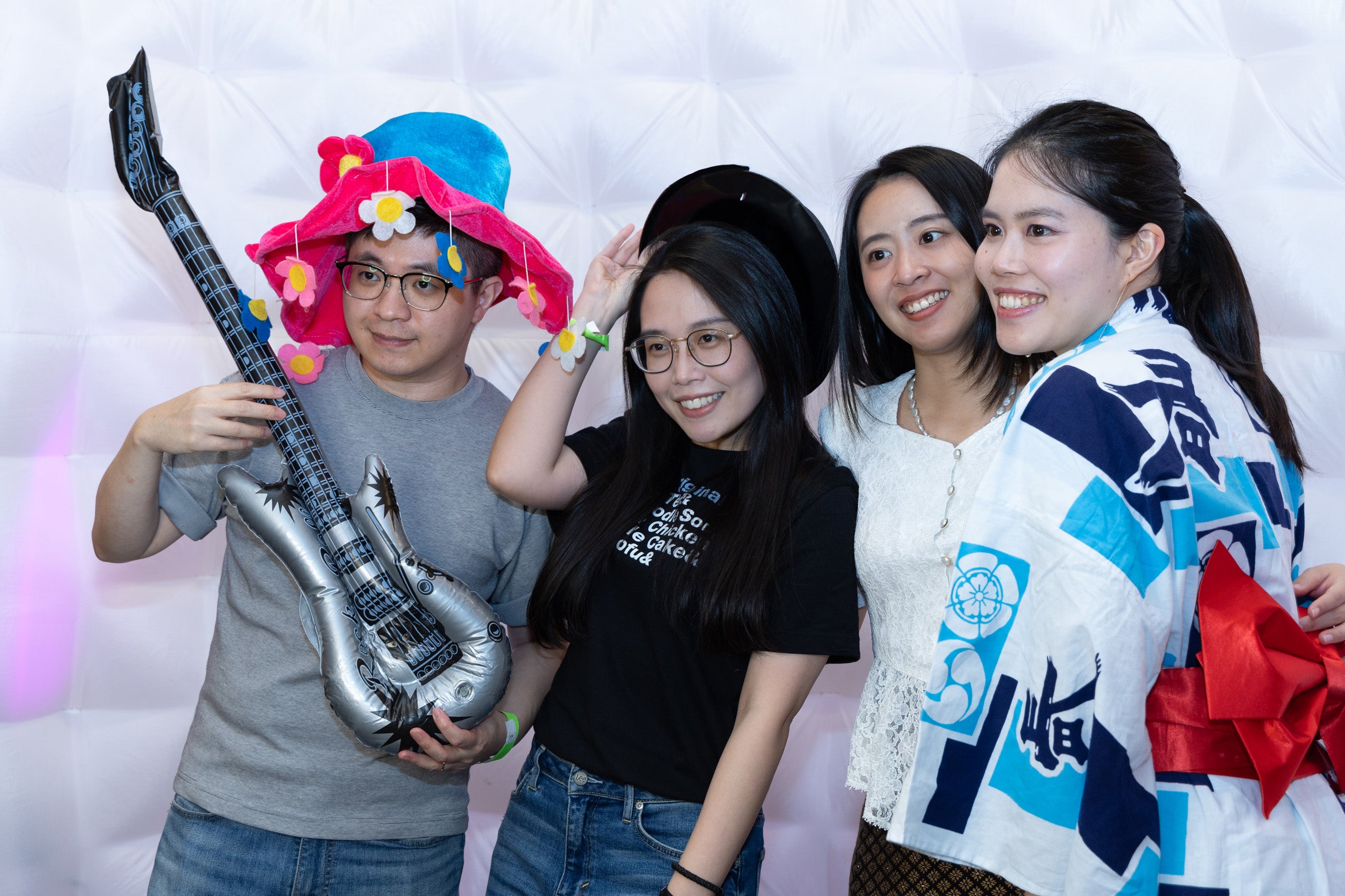 Three women and one man hold a guitar prop pose for the camera in a photo booth.