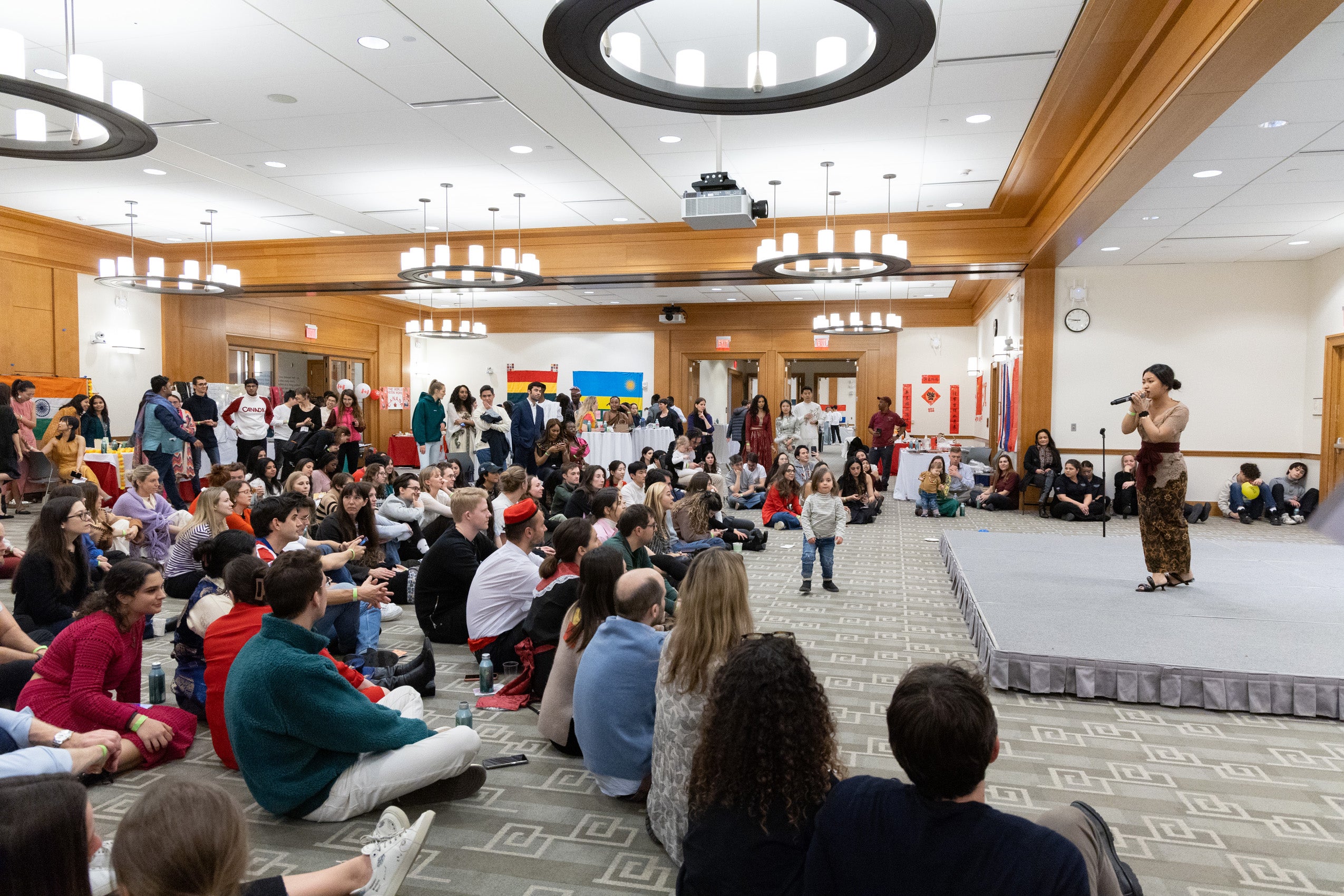 A student sings on the stage in front of a large group of students sitting on the ground watching.