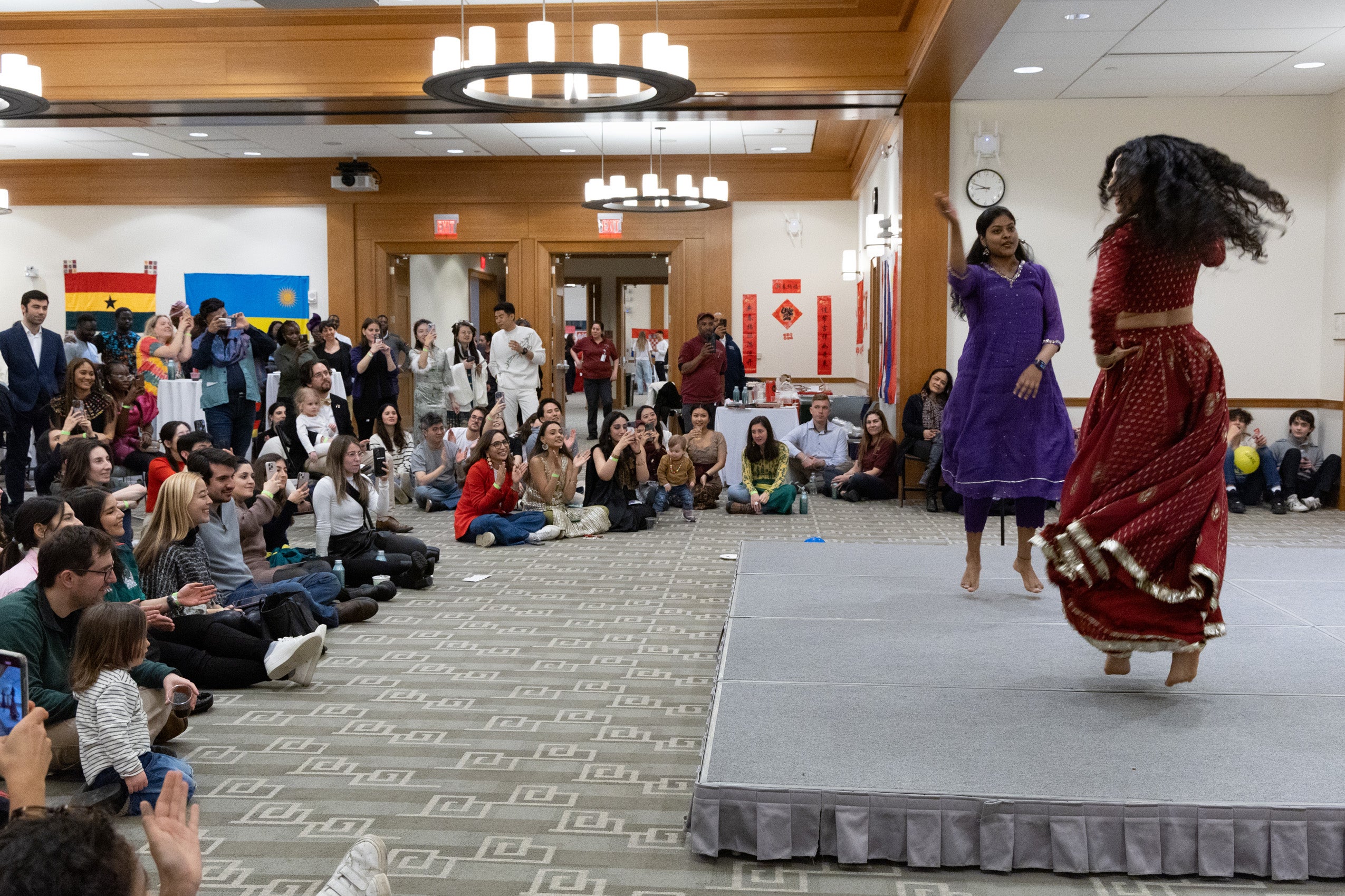 Two students dancing on a stage in front of a crowd of other students sitting around the stage.