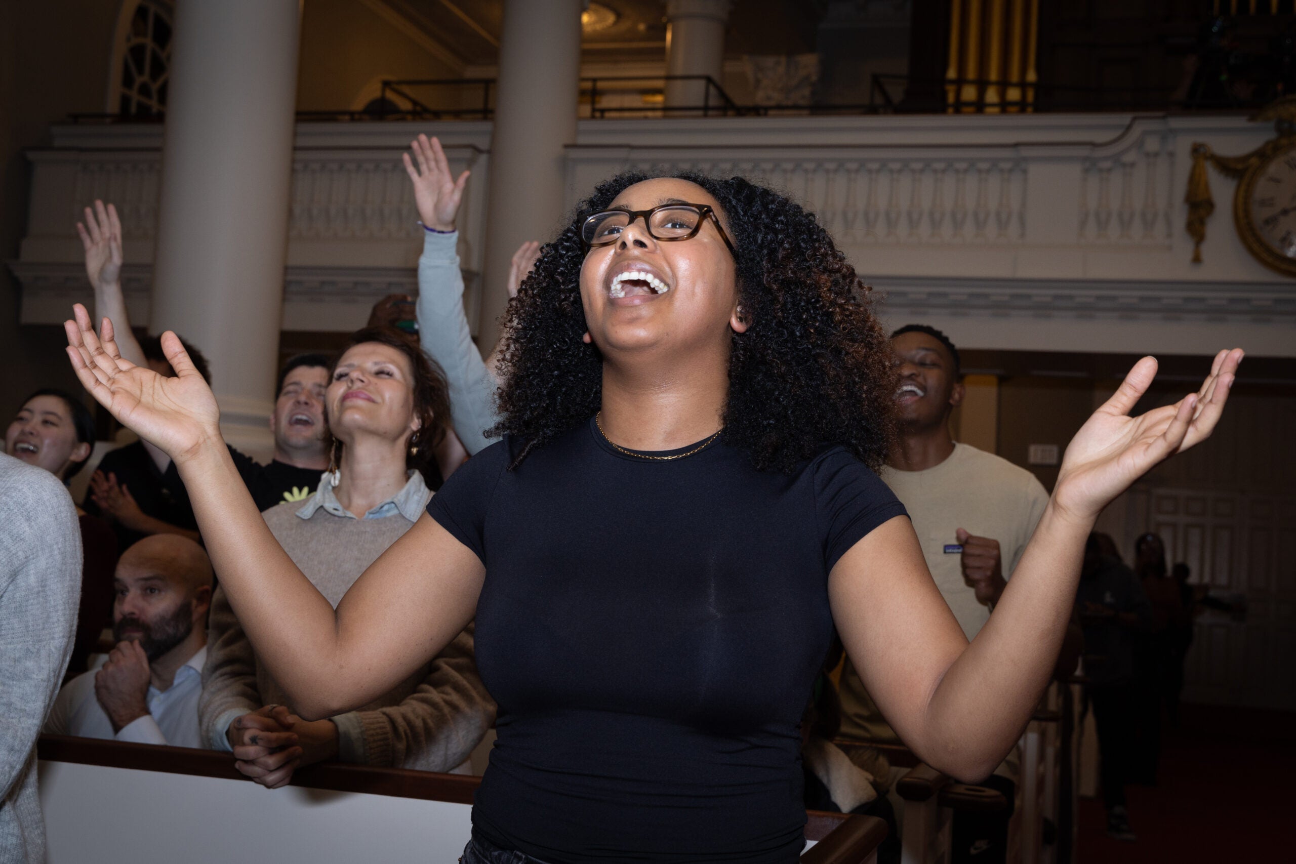 Woman with glasses sings with arms outstretched