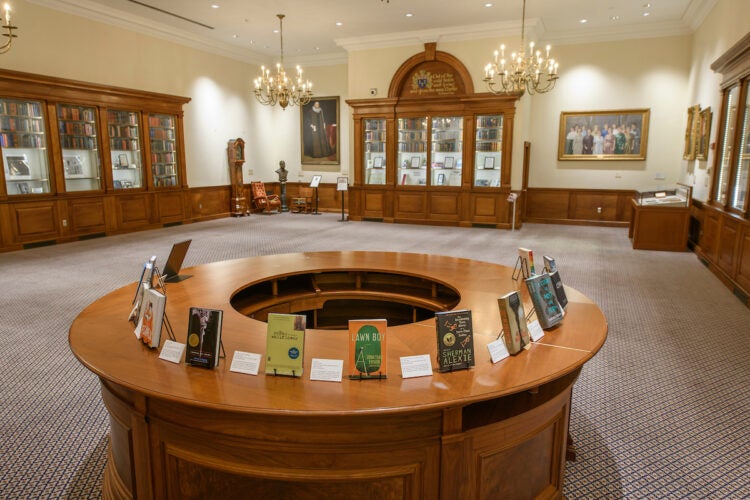 Caspersen Room with circular desk with books on top in the foreground. Room with paintings, historical furniture, adn built in bookcases.
