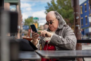 Actor impersonating Benjamin Franklin using a phone.