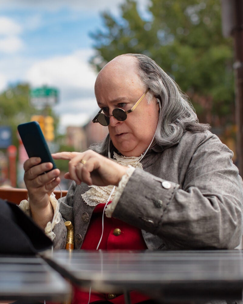 Actor impersonating Benjamin Franklin using a phone.
