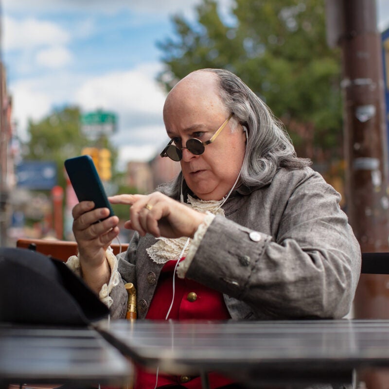 Actor impersonating Benjamin Franklin using a phone.