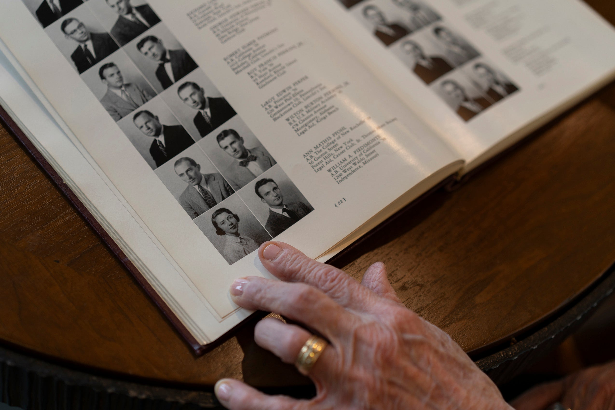A yearbook opened to a page with headshots and hand pointing to the headshot of the woman on the page.