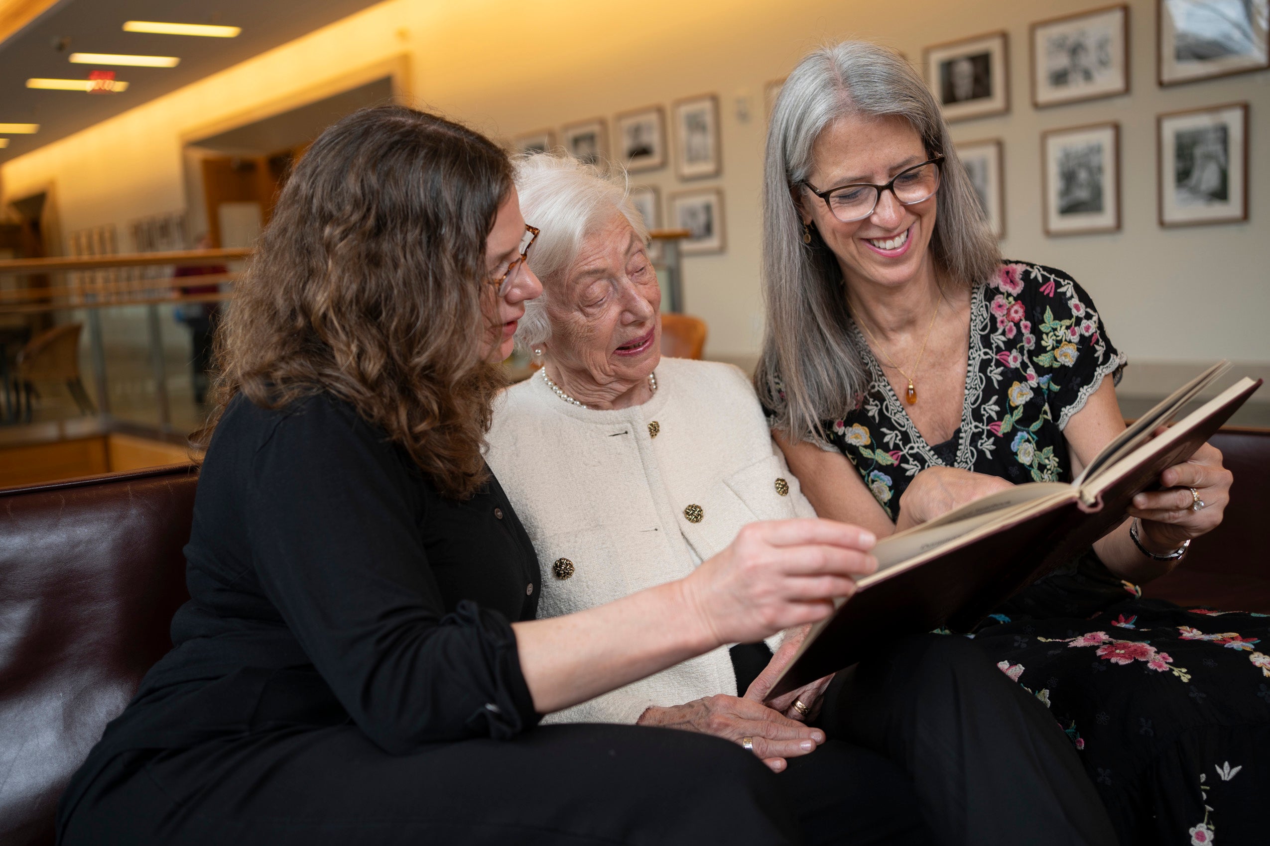 Three women sitting on a couch looking at a yearbook together.