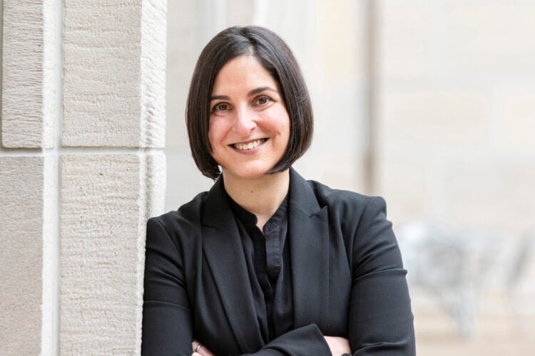 Portrait of woman wearing a black suit leaning against a gray building