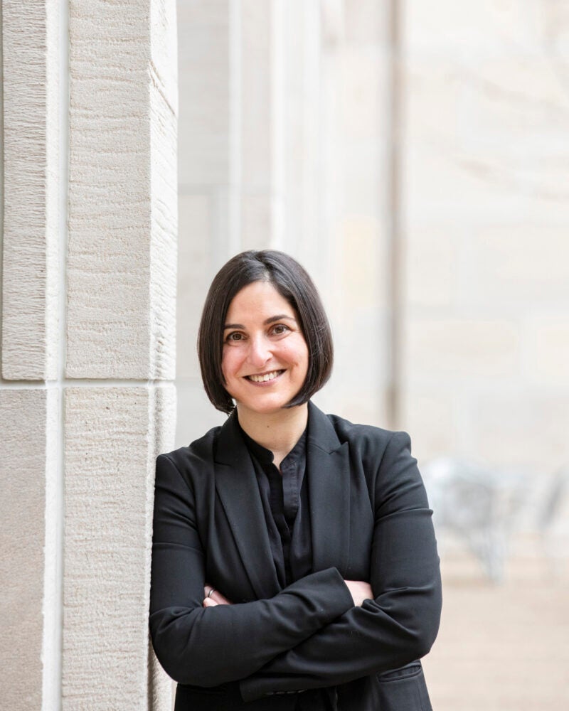 Portrait of woman wearing a black suit leaning against a gray building
