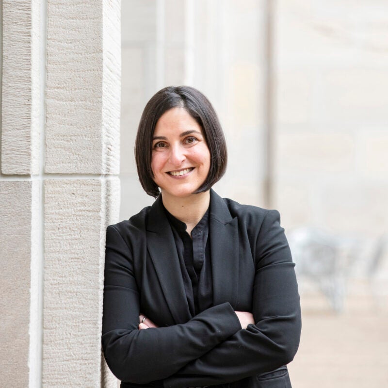 Portrait of woman wearing a black suit leaning against a gray building